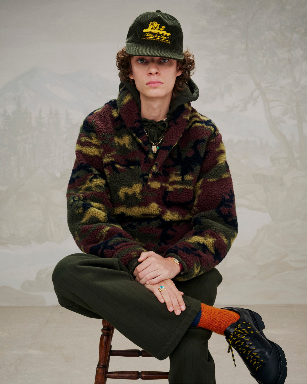 Person wearing a camo fleece jacket and Leather Derby Hiker shoes, sitting on a wooden chair.