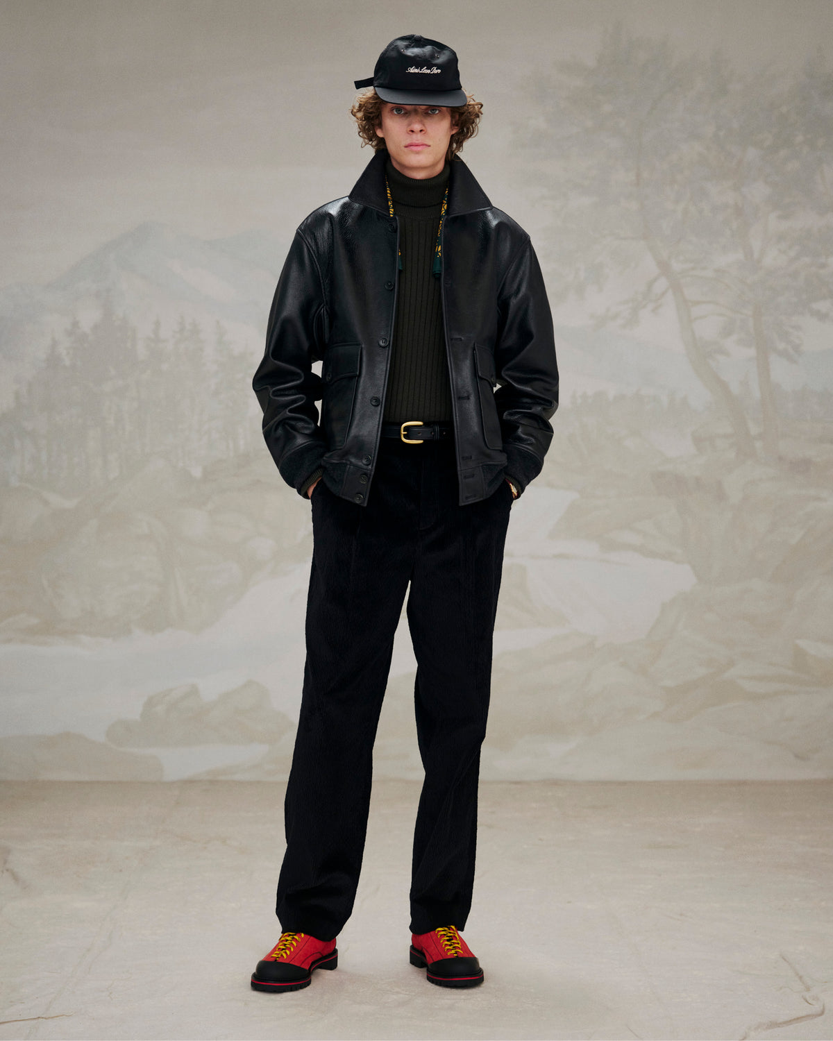 Person styled in a black leather jacket, black pants, and Suede Derby Hiker shoes before a muted landscape backdrop.