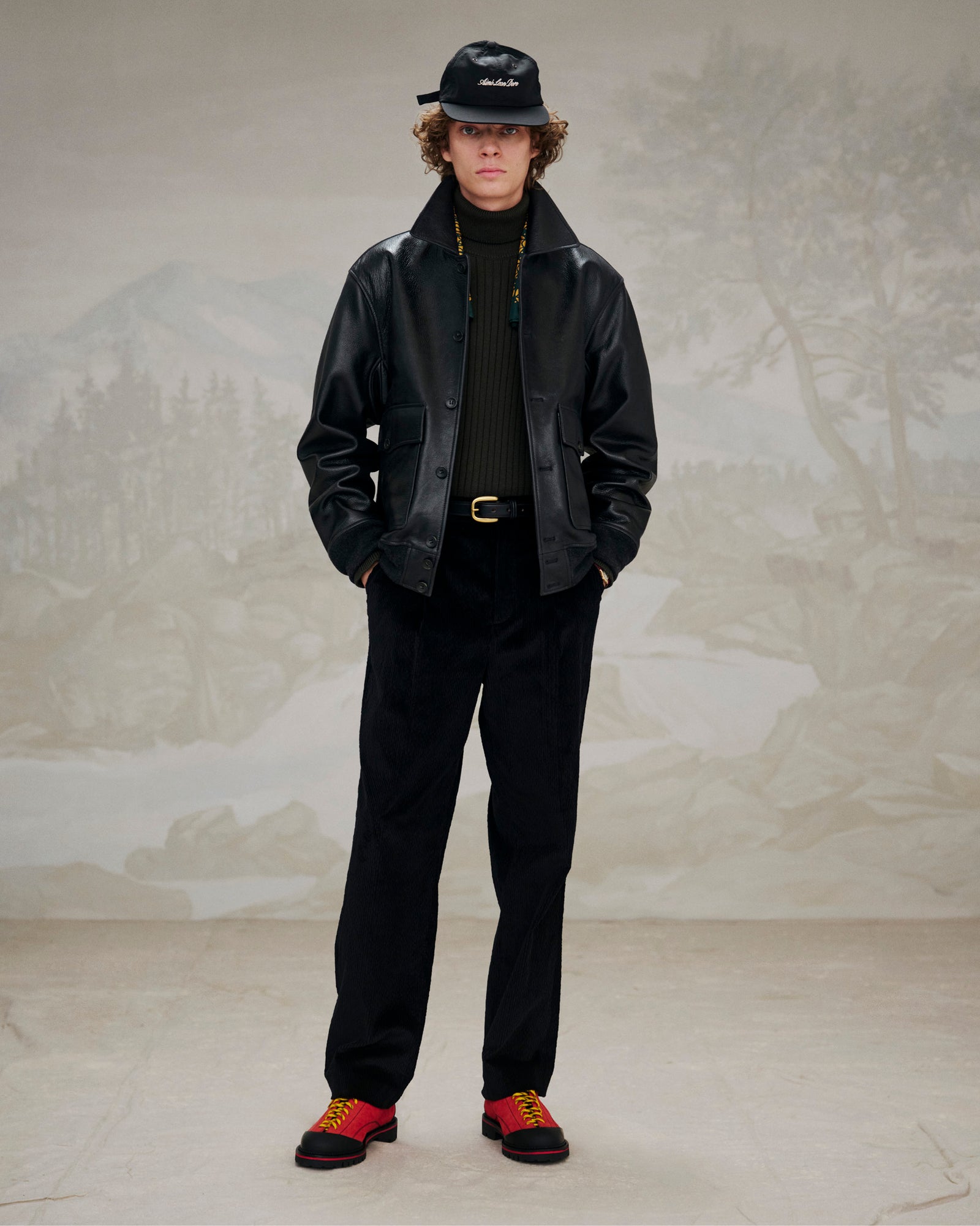 Person styled in a black leather jacket, black pants, and Suede Derby Hiker shoes before a muted landscape backdrop.