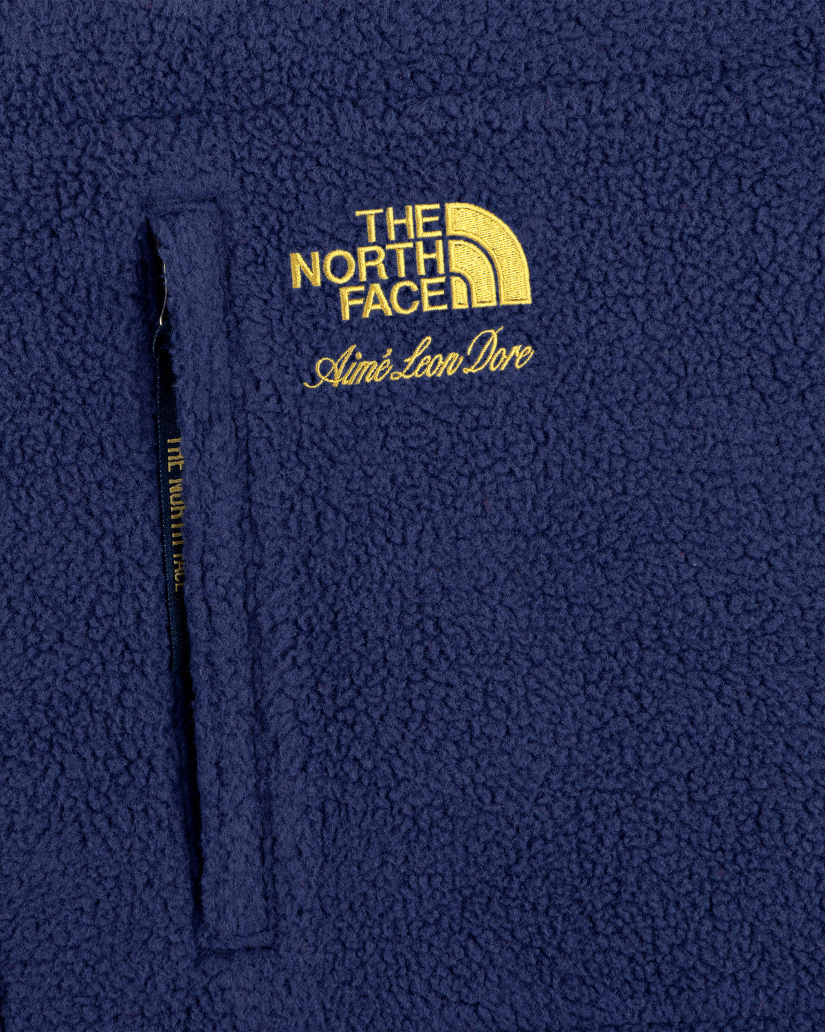 Navy blue ALD/The North Face packable fleece blanket with zip pocket and yellow embroidered logo.