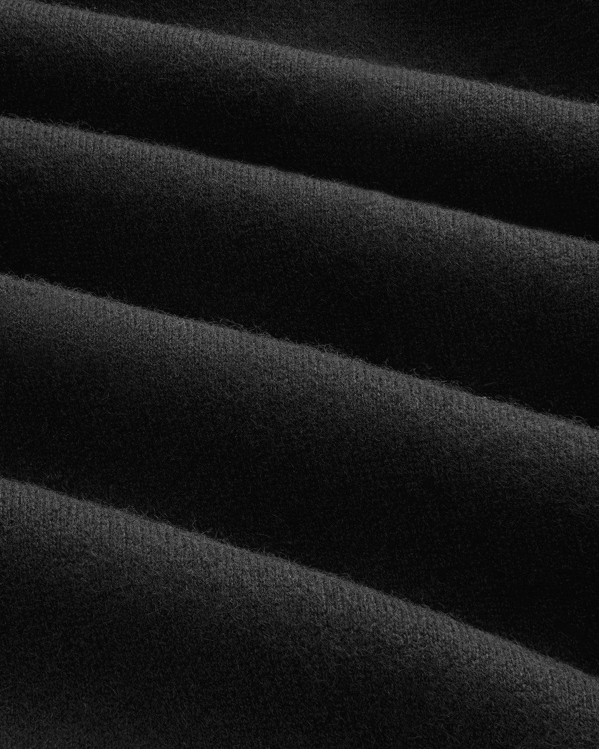 Close-up of soft, black Pavilion Cashmere Hoodie fabric with ridges and diagonal folds creating texture.