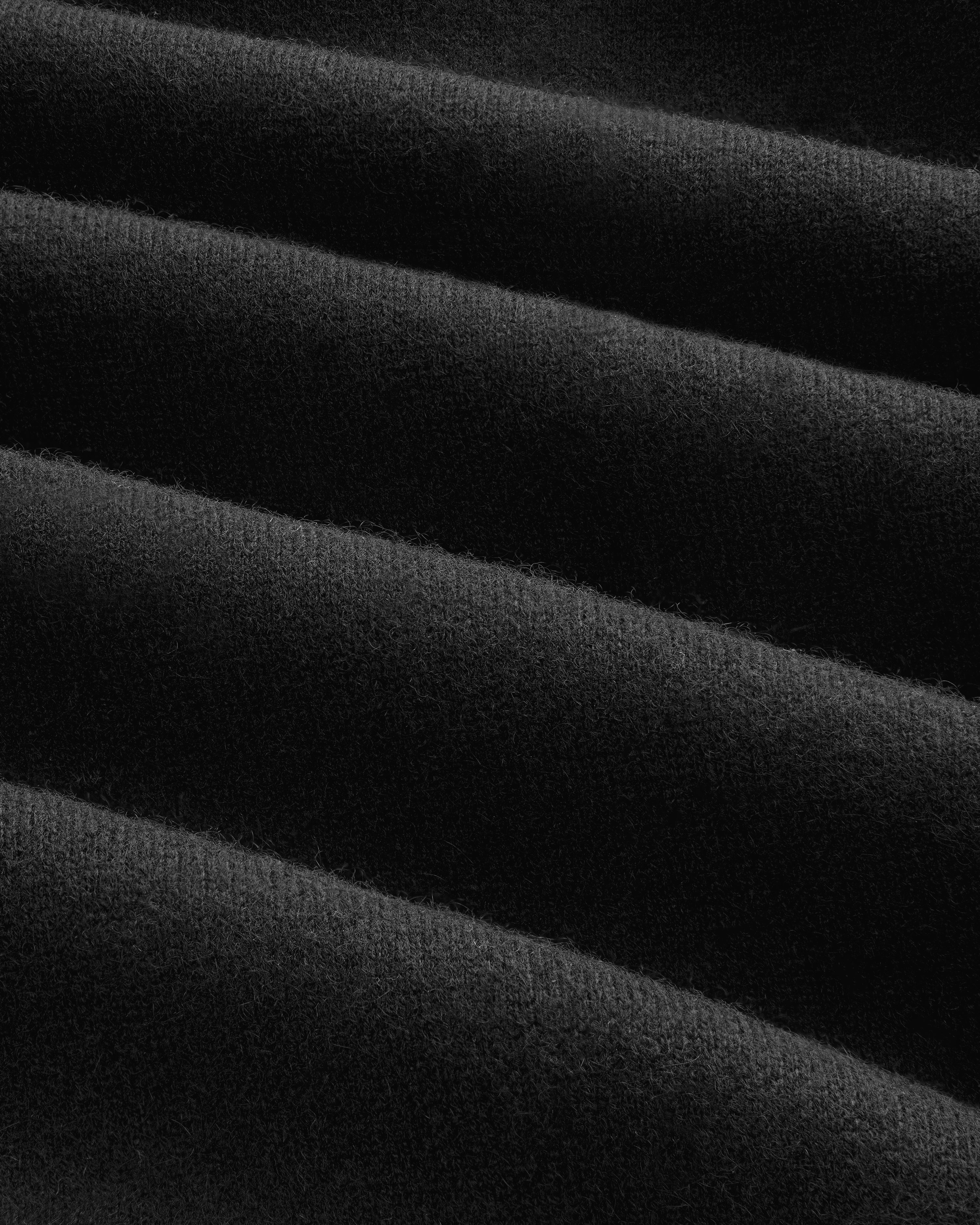 Close-up of soft, black Pavilion Cashmere Hoodie fabric with ridges and diagonal folds creating texture.