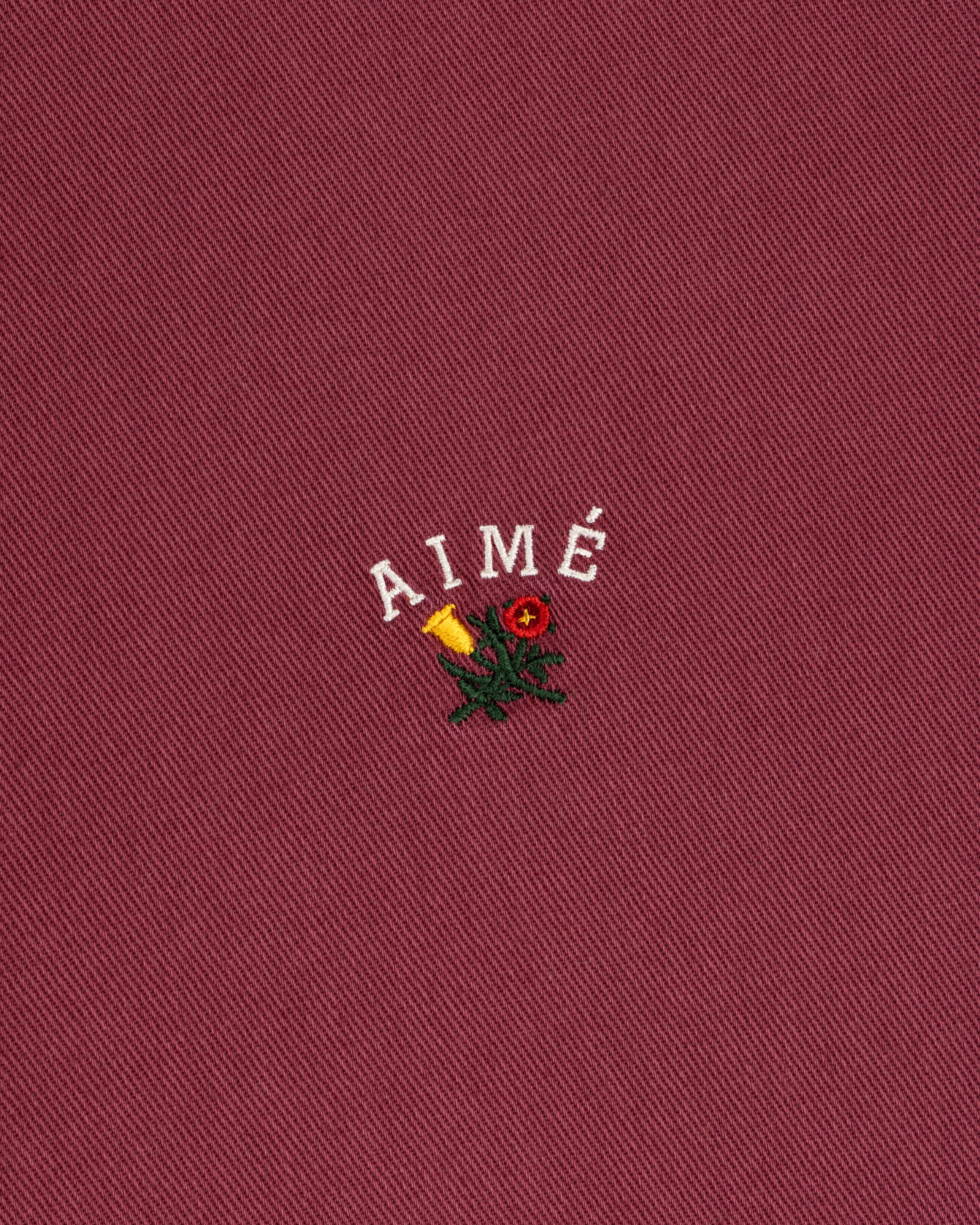 Garment Dyed Leon Overshirt: red with white AIMÉ text, yellow rose, and green leaves embroidery.