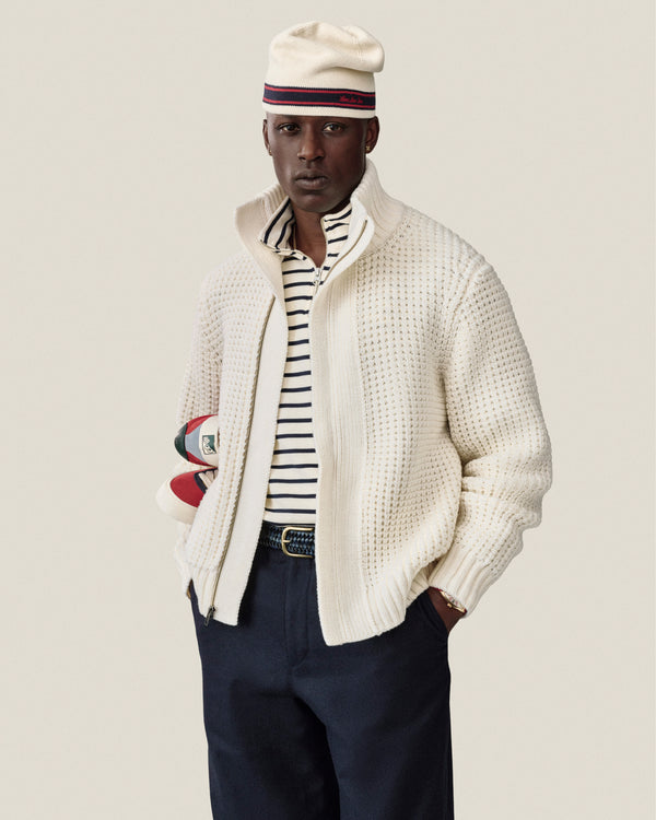 A man in a Striped Crest Quarter Zip and beret holds rugby balls against a plain background.