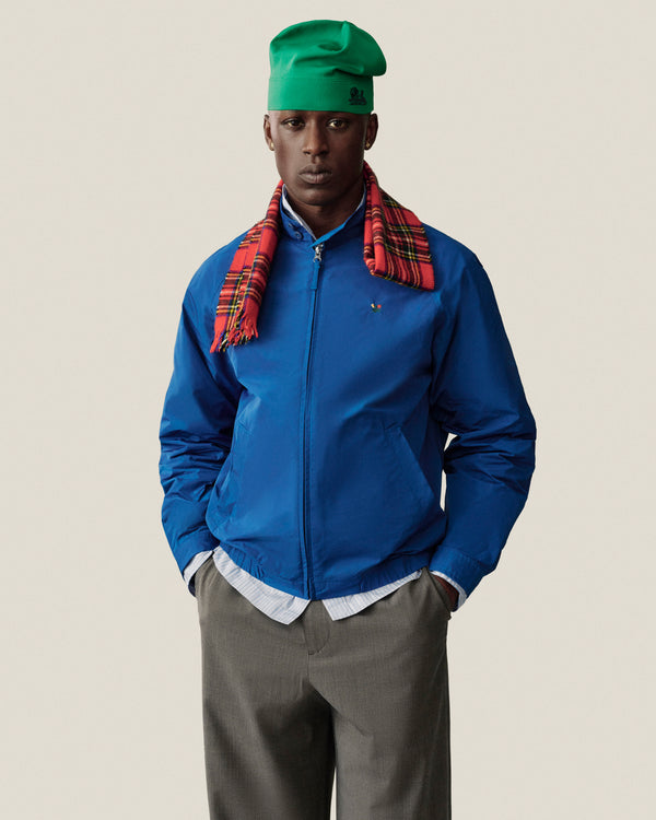 Man in blue jacket, green hat, and red plaid scarf poses in Houndstooth Elasticated Waist Trouser against plain backdrop.
