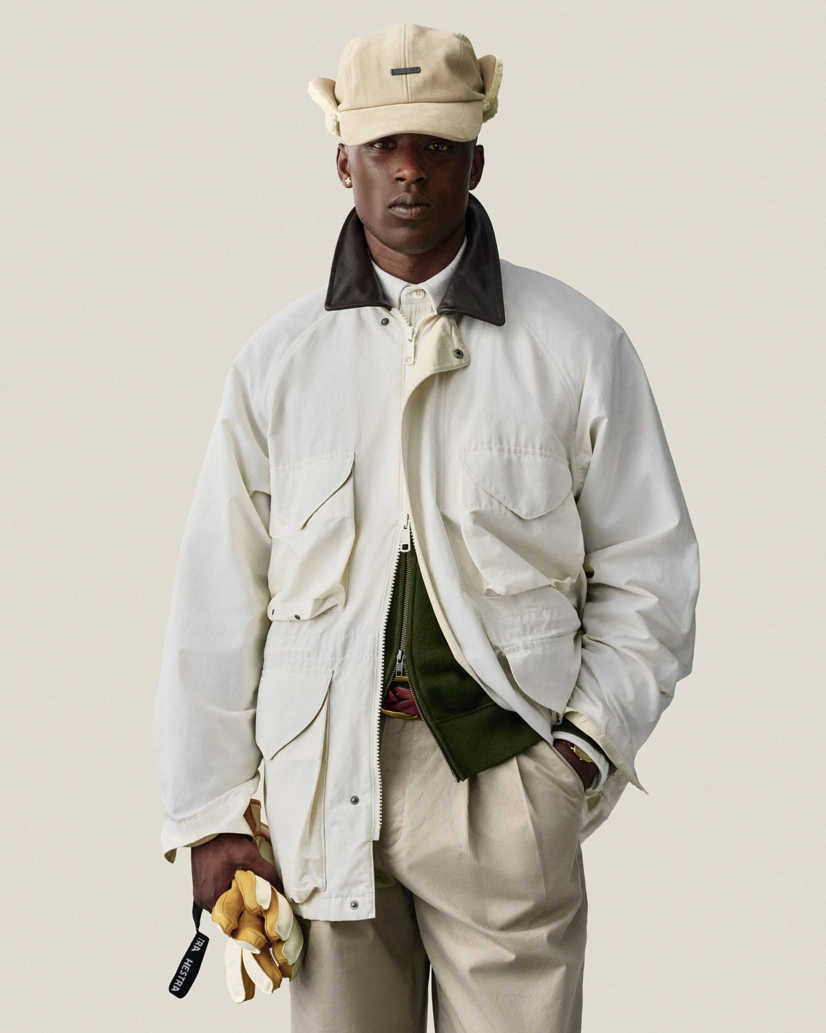 A man in a Lightweight Barn Jacket, beige cap, and tan pants holds yellow gloves against a plain background.