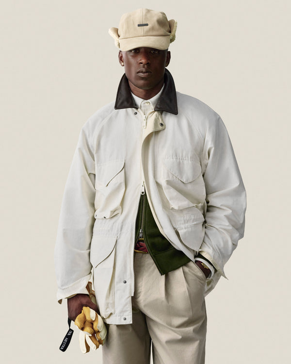 A man in a Lightweight Barn Jacket, beige cap, and tan pants holds yellow gloves against a plain background.