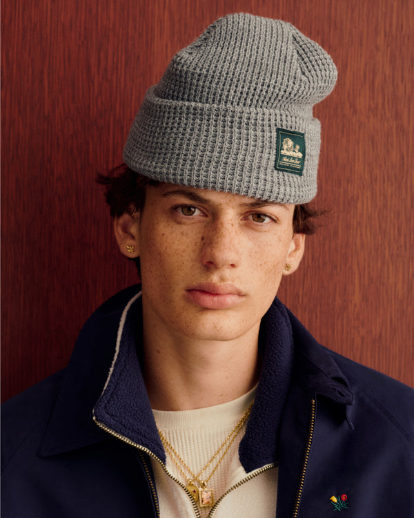 Young person in Crest Casual Jacket and gray knit beanie, with gold jewelry, against a wooden background.