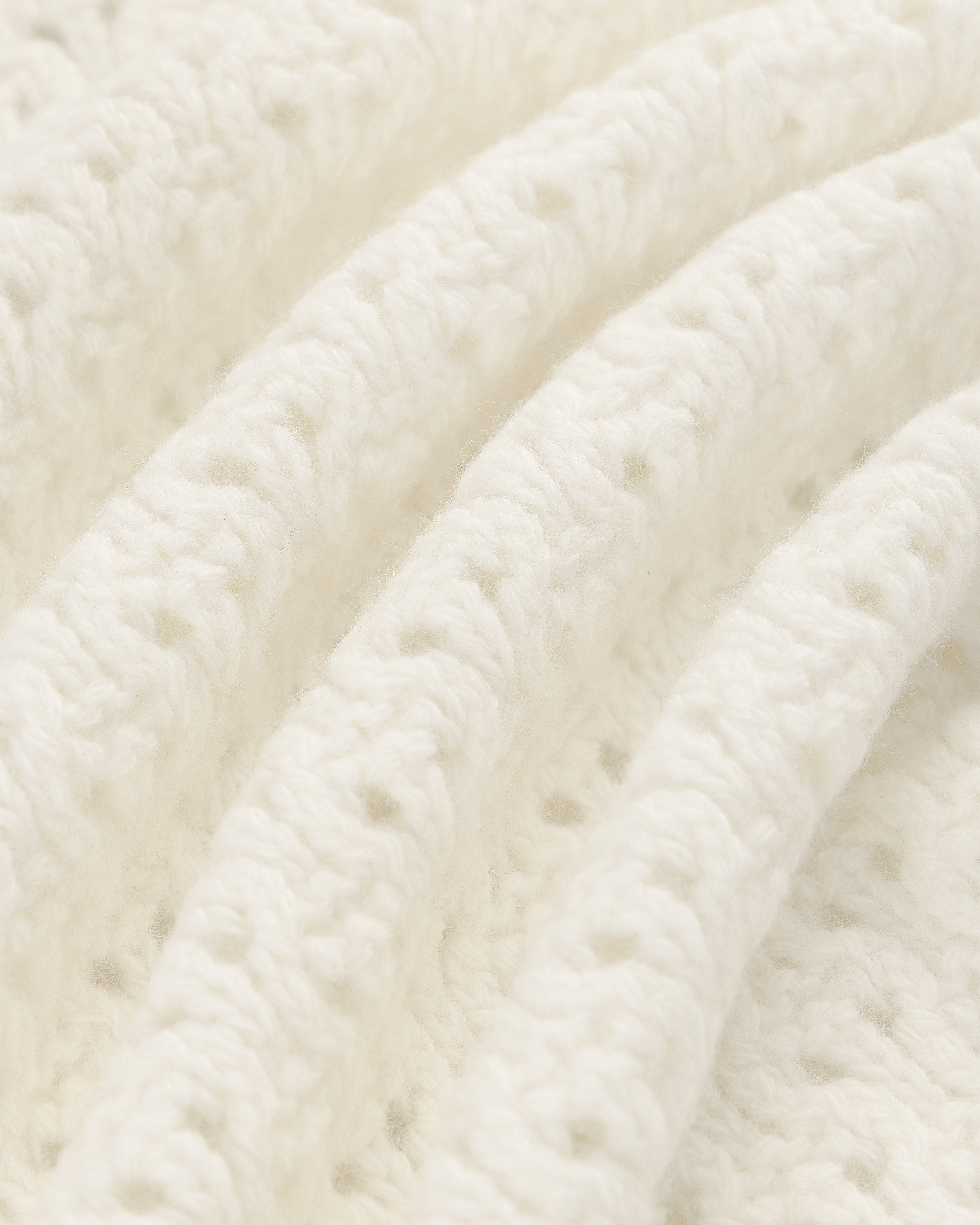 Close-up of Knit Polo Cardigan’s soft, white knit fabric with gentle folds and visible yarn texture.