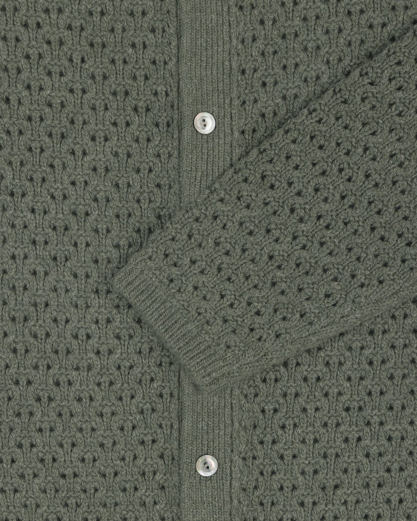 Close-up of a green Knit Polo Cardigan with silver buttons and a sleeve draped diagonally across the center.