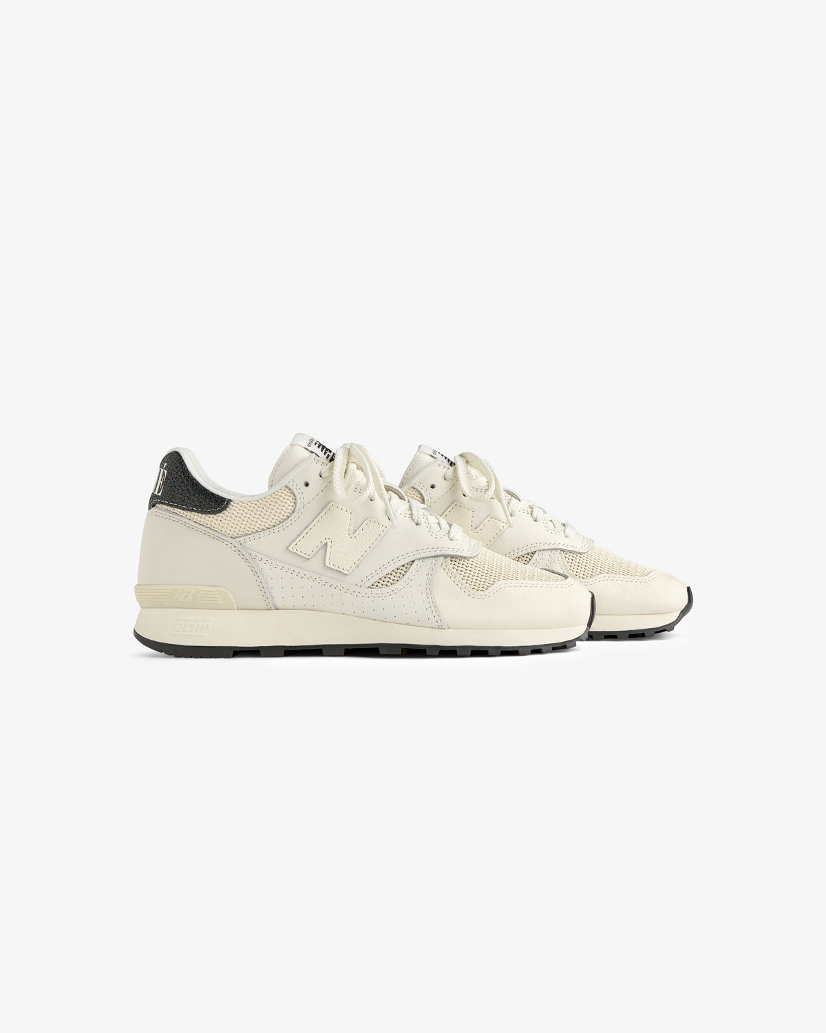 ALD / New Balance 475 sneakers in off-white with black heel accents, shown side by side on a white background.