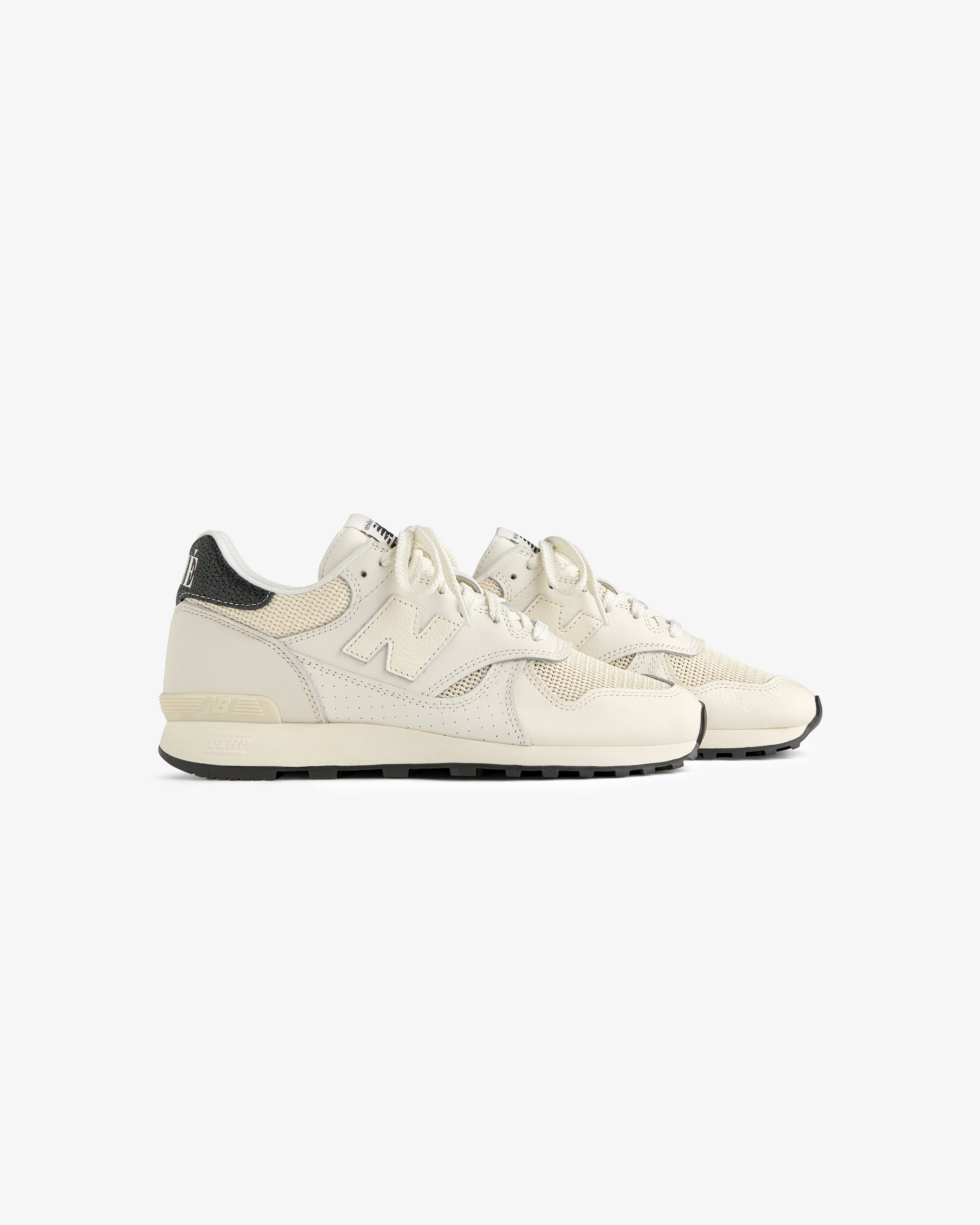 ALD / New Balance 475 sneakers in off-white with black heel accents, shown side by side on a white background.