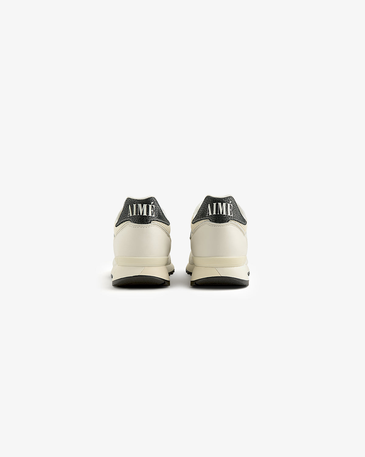 Back view of two ALD / New Balance 475 cream sneakers with dark gray heels and AIMÉ text, on a white background.
