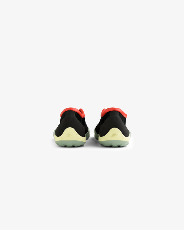 The ALD / New Balance MT10T Sport Shoe features black uppers, yellow-green soles, and red accents, seen from the back.
