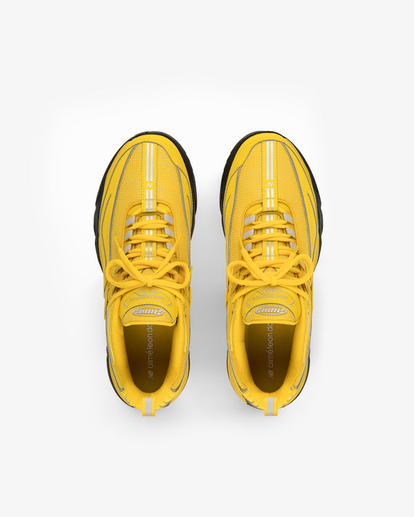 A pair of ALD / New Balance RC56 yellow athletic sneakers with black soles, viewed from above on white.