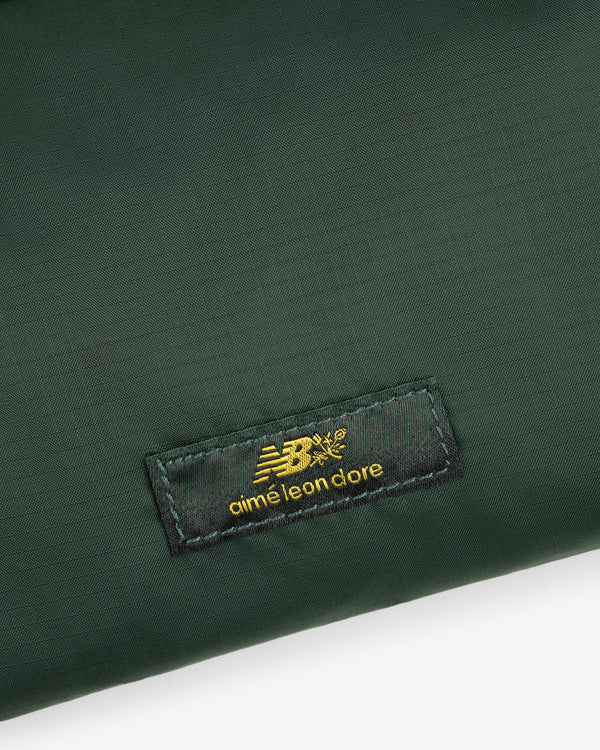 Close-up of a green ALD / New Balance Nylon Sling Pouch with a black patch featuring gold New Balance aimé leon dore text.