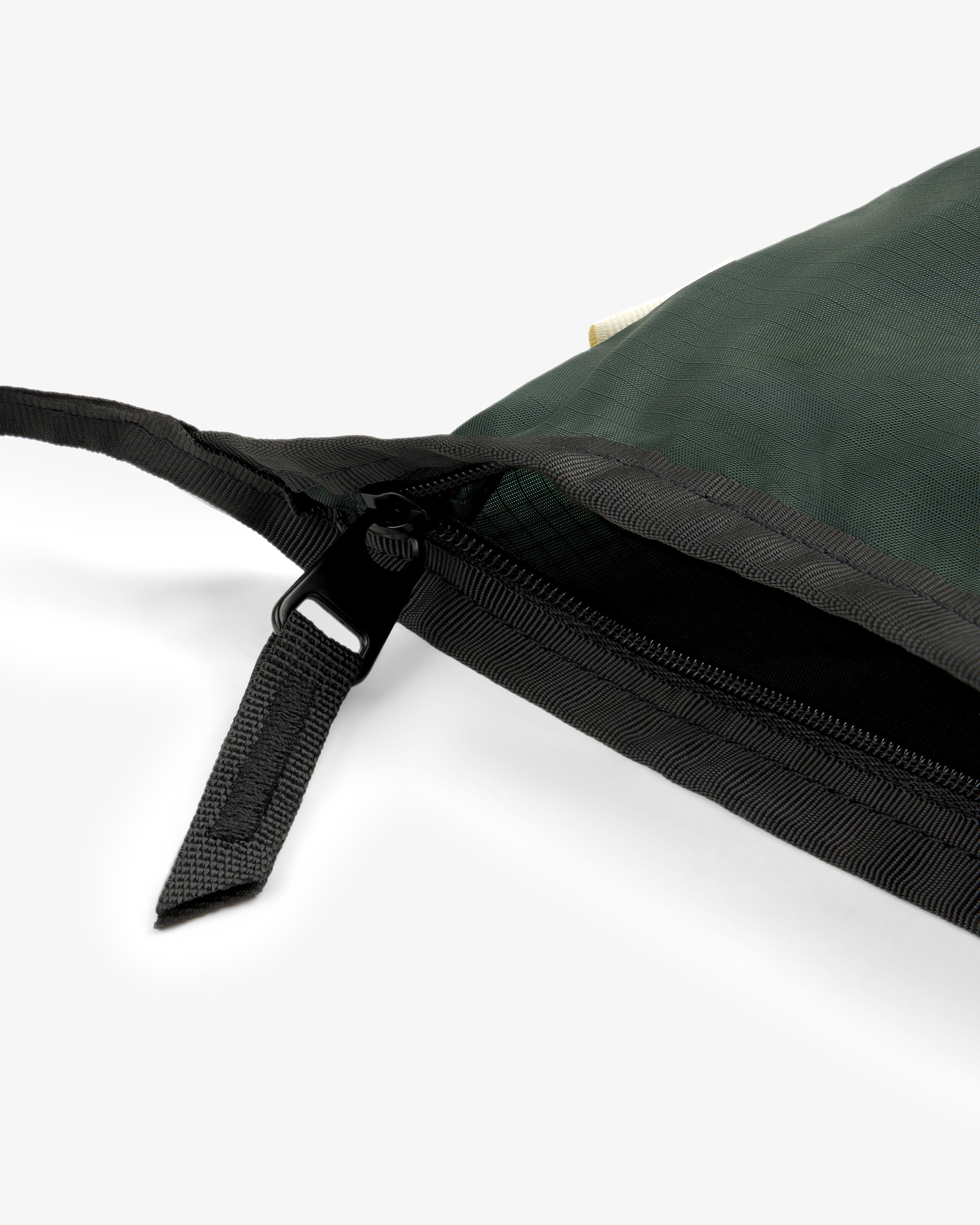 Close-up of a black zipper on the ALD / New Balance Nylon Sling Pouch in dark green, partially unzipped.