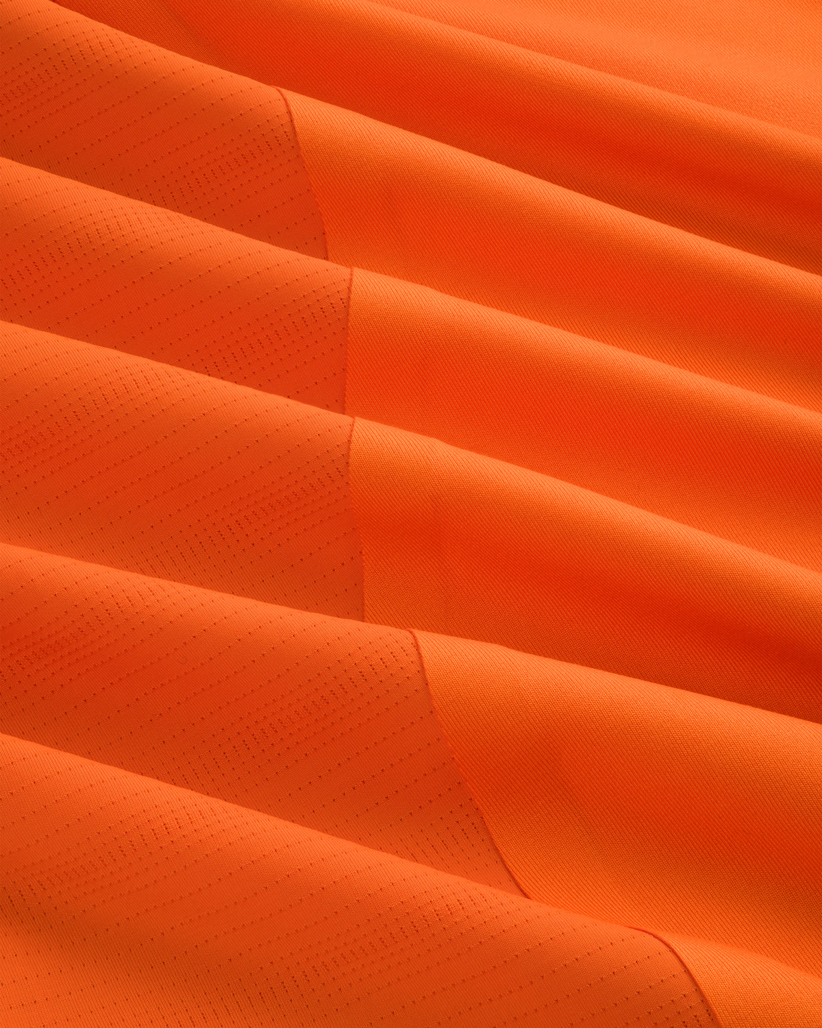 Close-up of the ALD / New Balance Performance Long-Sleeve Tee's orange fabric with diagonal lines and textured folds.