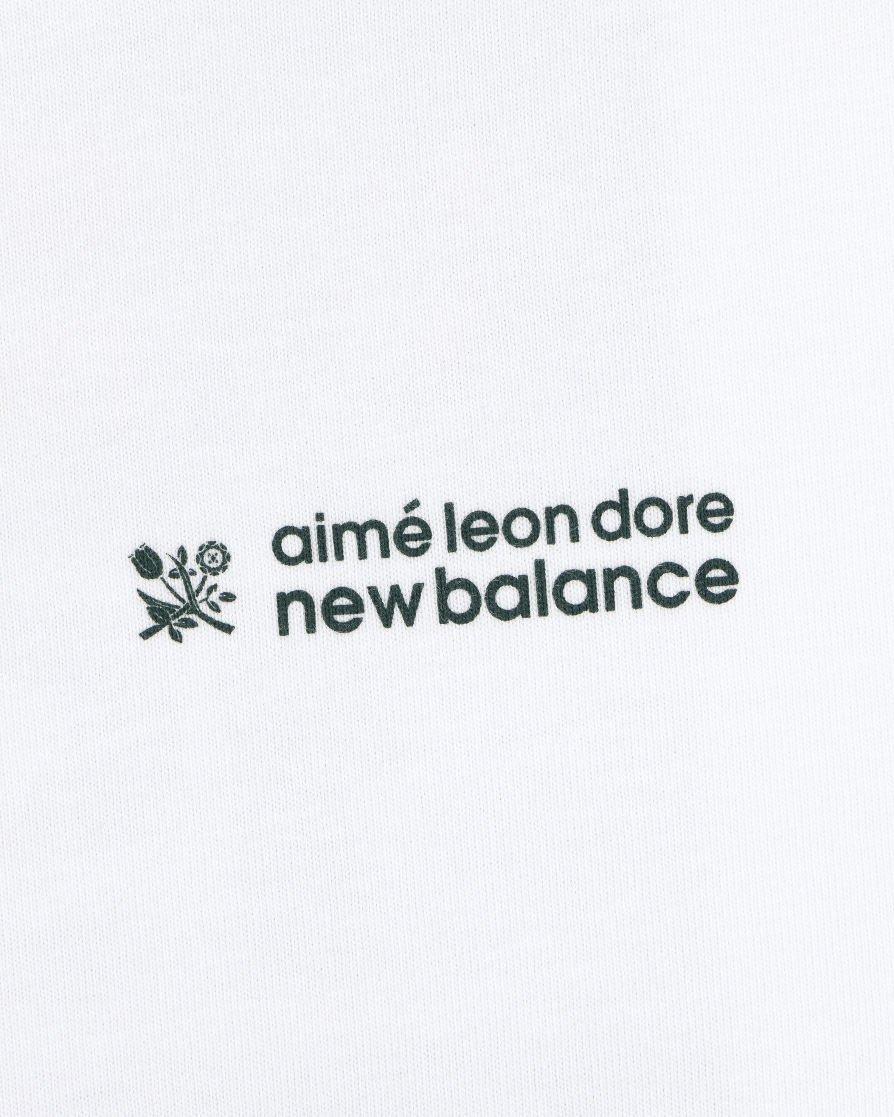 Black ALD / New Balance Running Bib Tee with logo and small flower graphic on white fabric background.