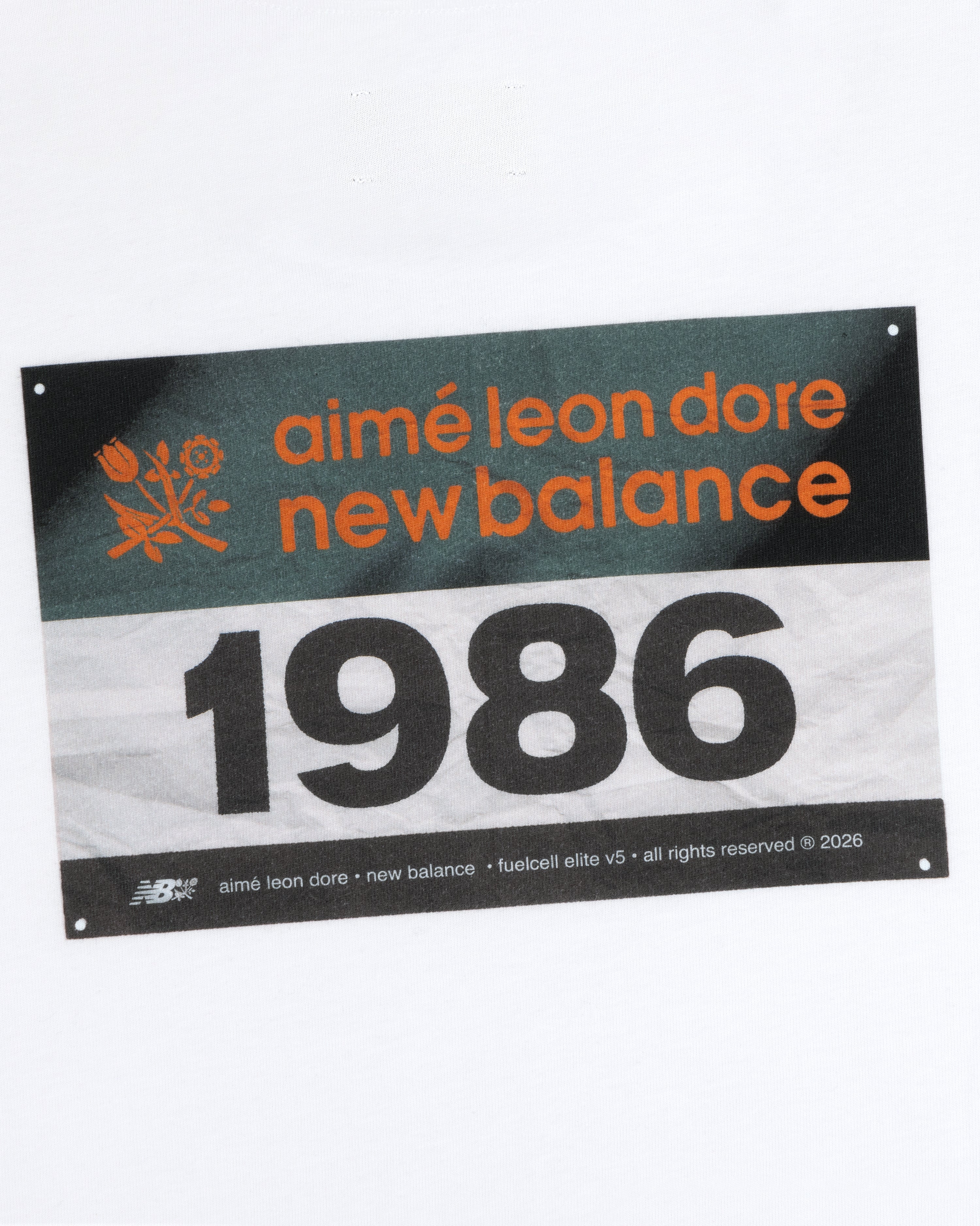 Rectangular label on white with "ALD / New Balance Running Bib Tee" and the number 1986.