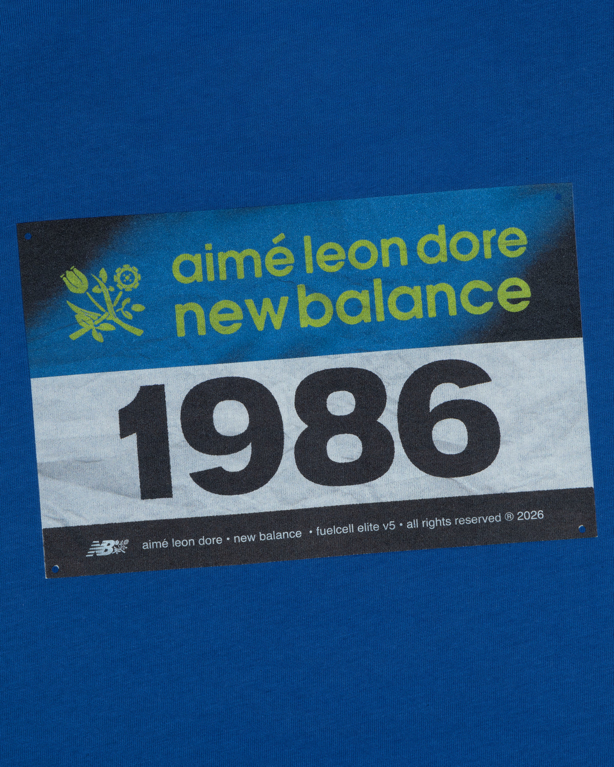 The ALD / New Balance Running Bib Tee features a blue race bib with "aimé leon dore" and 1986 printed on it.