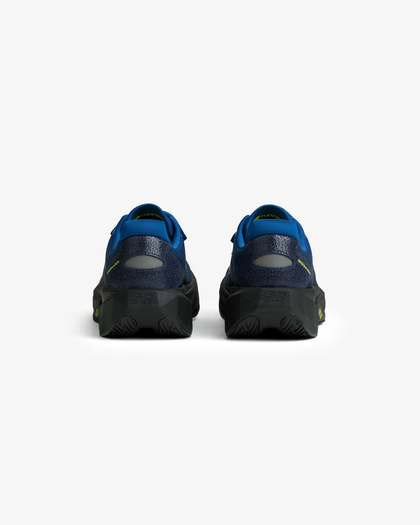 Rear view of ALD / New Balance FuelCell Rebel v5 in blue and black with textured soles on a white background.
