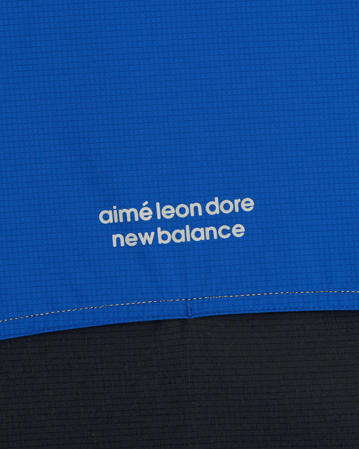 Close-up of blue ALD / New Balance Performance Nylon Jacket with white logo in lowercase letters.