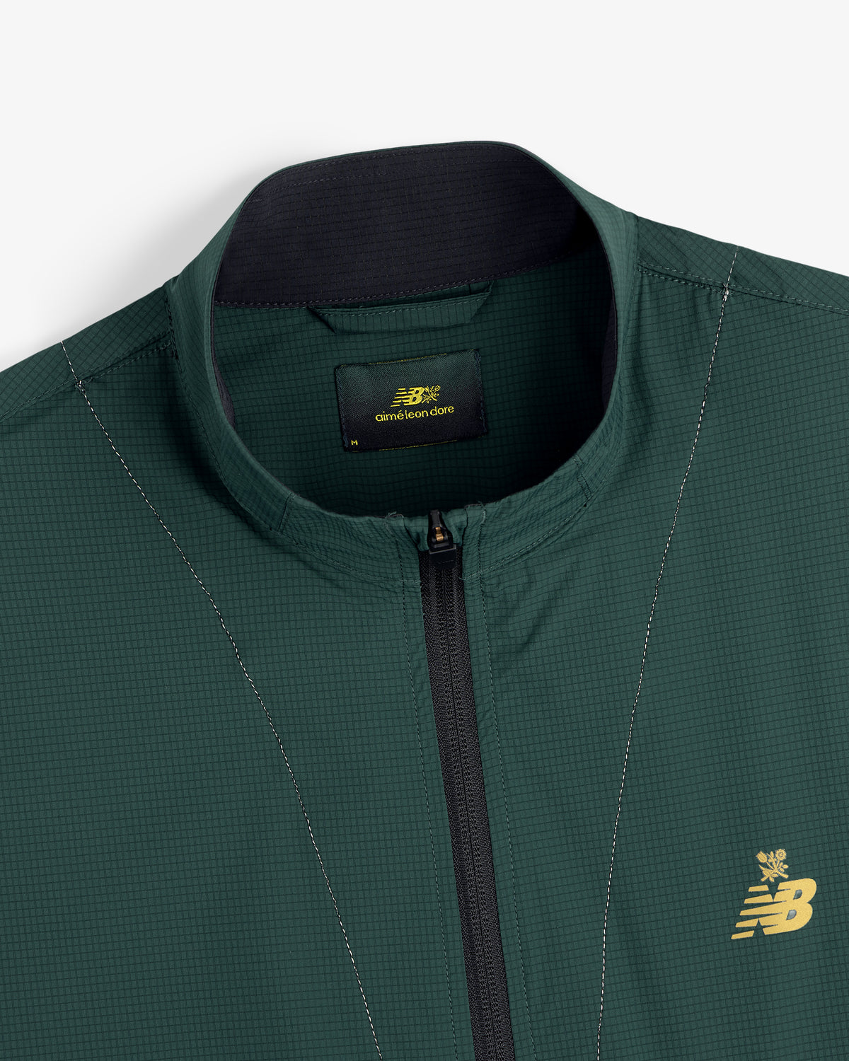 Close-up of the ALD / New Balance Performance Nylon Jacket in green with zip front and gold chest logo.