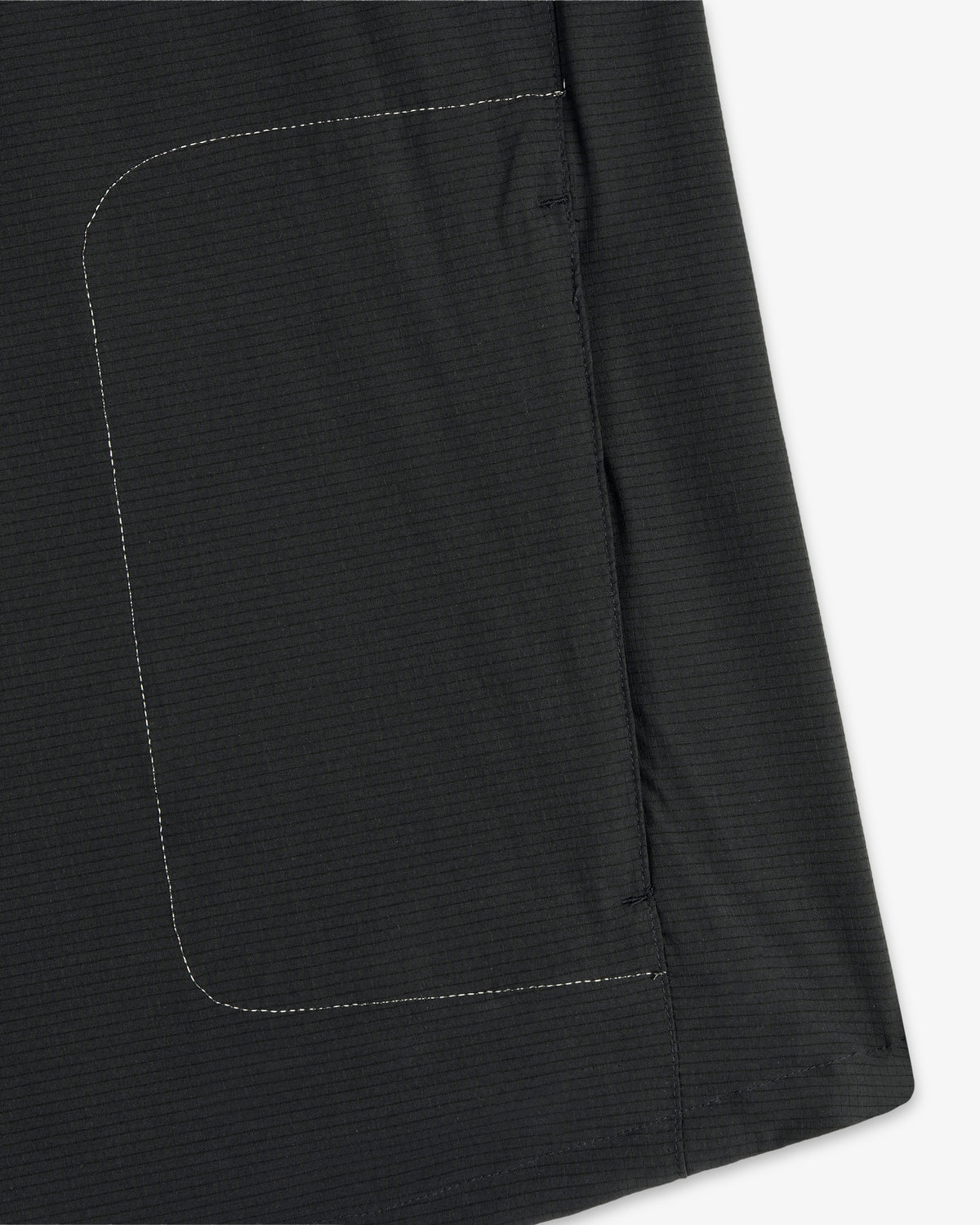 Close-up of a black pocket with white stitching on the ALD / New Balance Performance Nylon Jacket, against white.