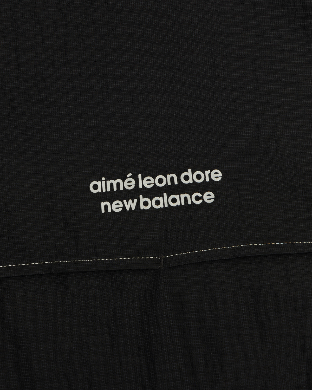 Close-up of black ALD / New Balance Breathable Half-Zip Pullover with white logo above a stitched seam.