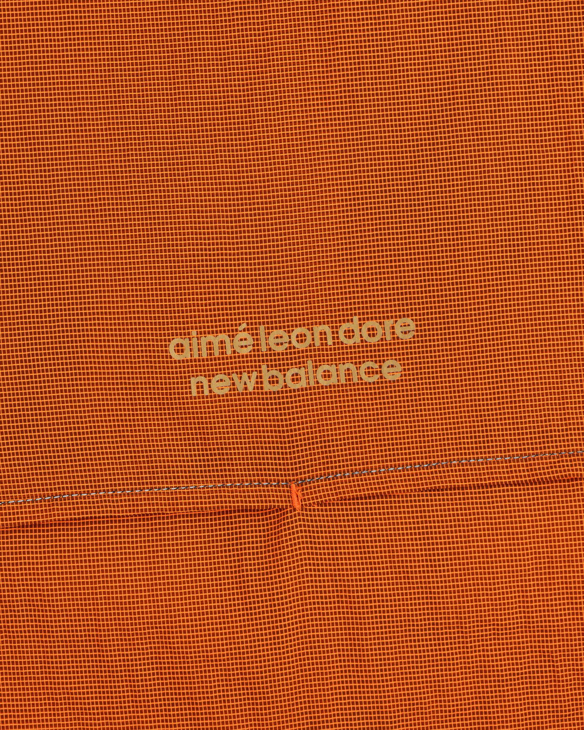 Orange grid-patterned ALD / New Balance Half-Zip Pullover with light yellow text at the center.