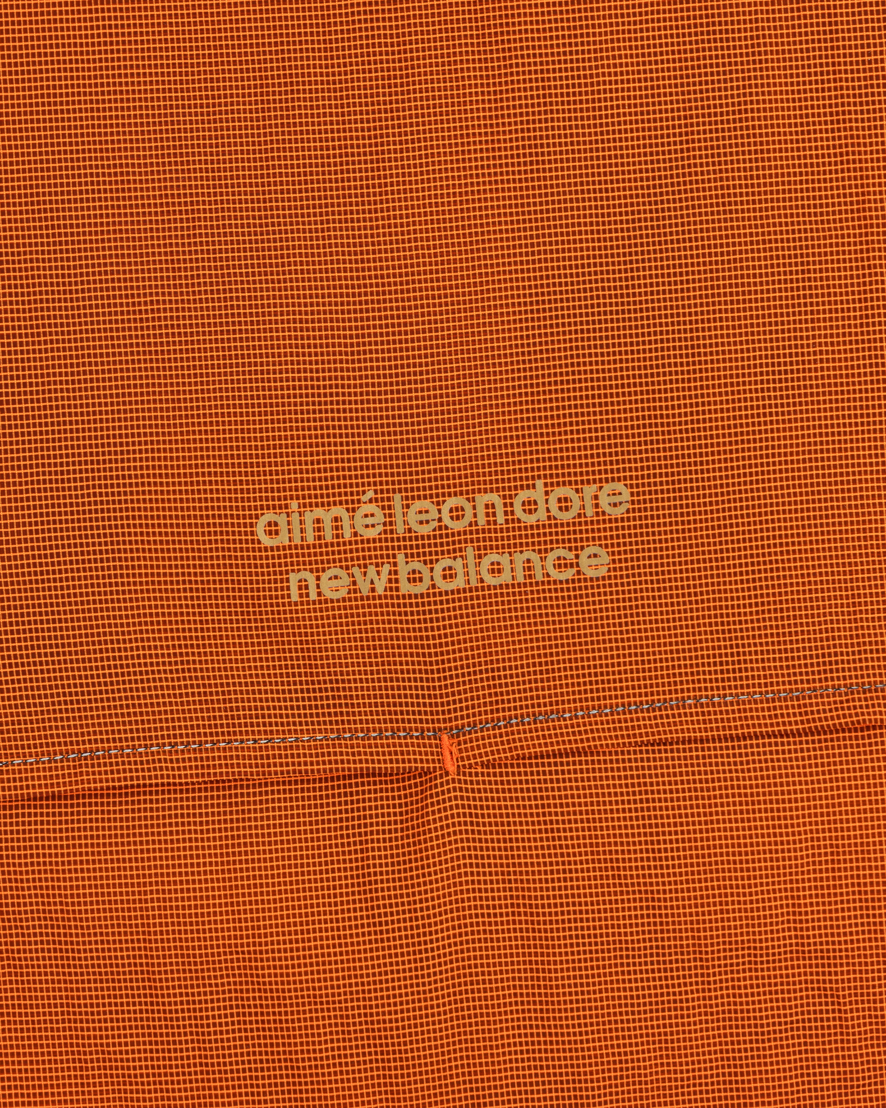 Orange grid-patterned ALD / New Balance Half-Zip Pullover with light yellow text at the center.