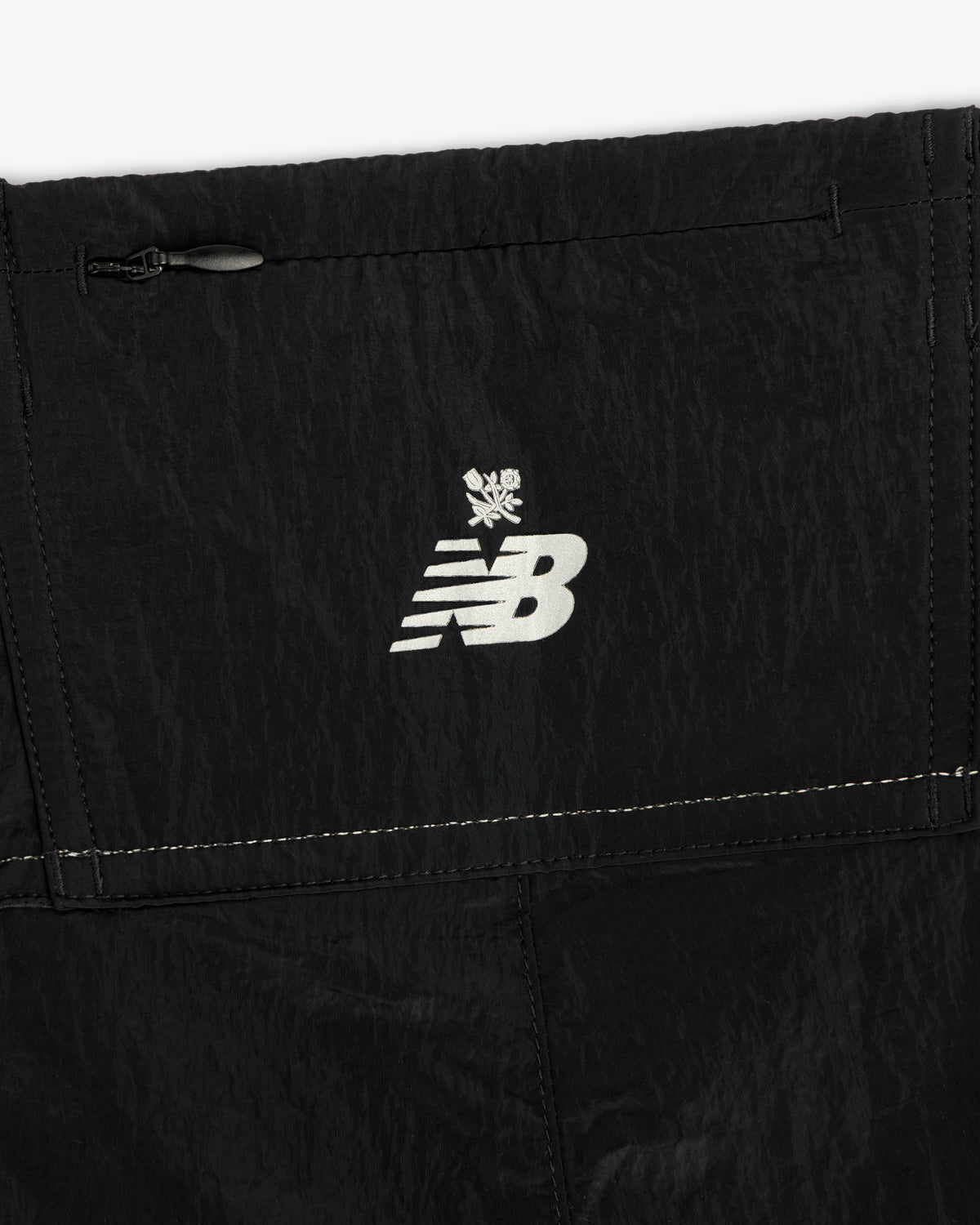 Close-up of the ALD / New Balance Lightweight Nylon Warmup Pant featuring a white logo and snowflake on black fabric.