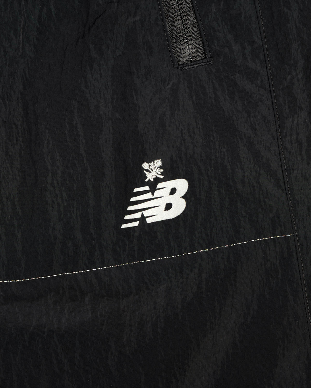 Close-up of black ALD / New Balance Lightweight Nylon Warmup Pant with white logo and small snowflake above it.