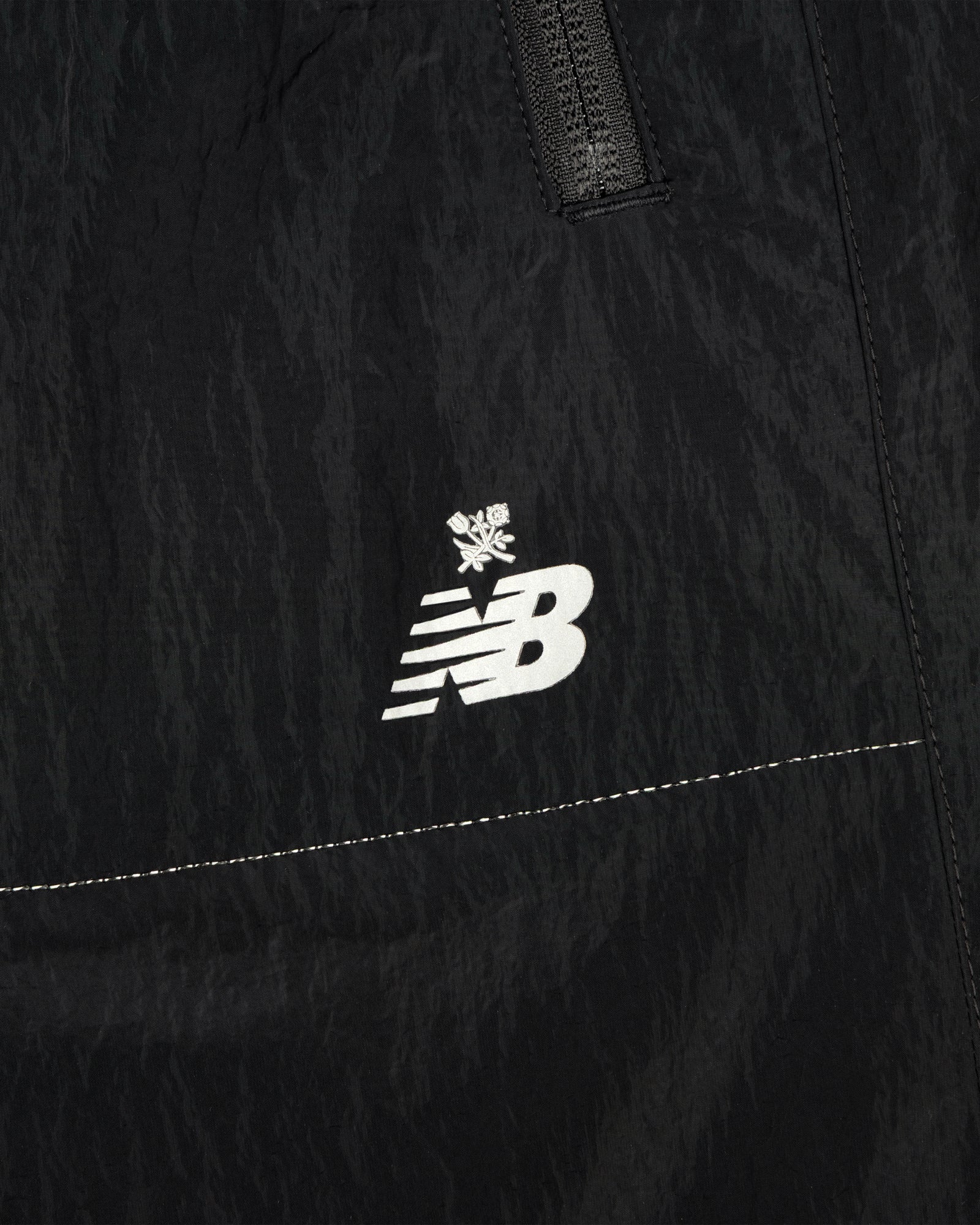Close-up of black ALD / New Balance Lightweight Nylon Warmup Pant with white logo and small snowflake above it.