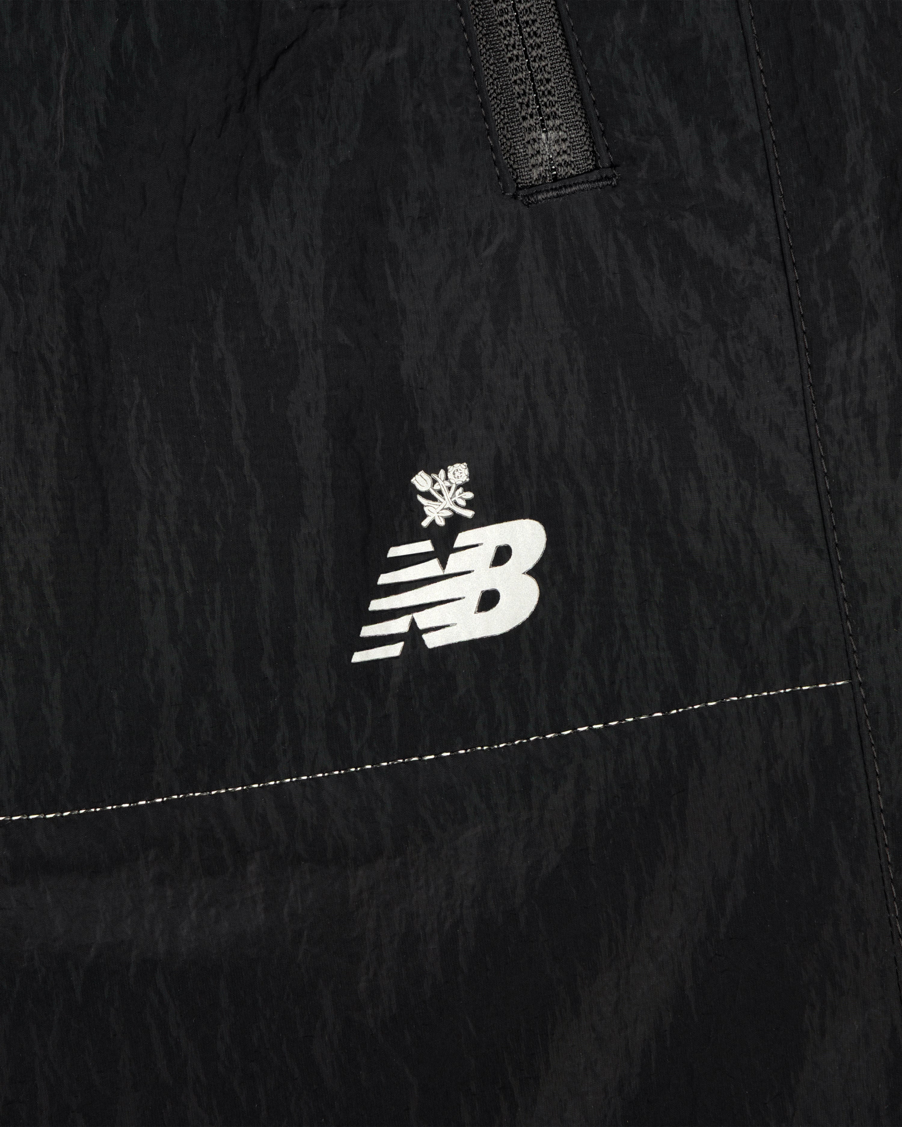 Close-up of black ALD / New Balance Lightweight Nylon Warmup Pant with white logo and small snowflake above it.