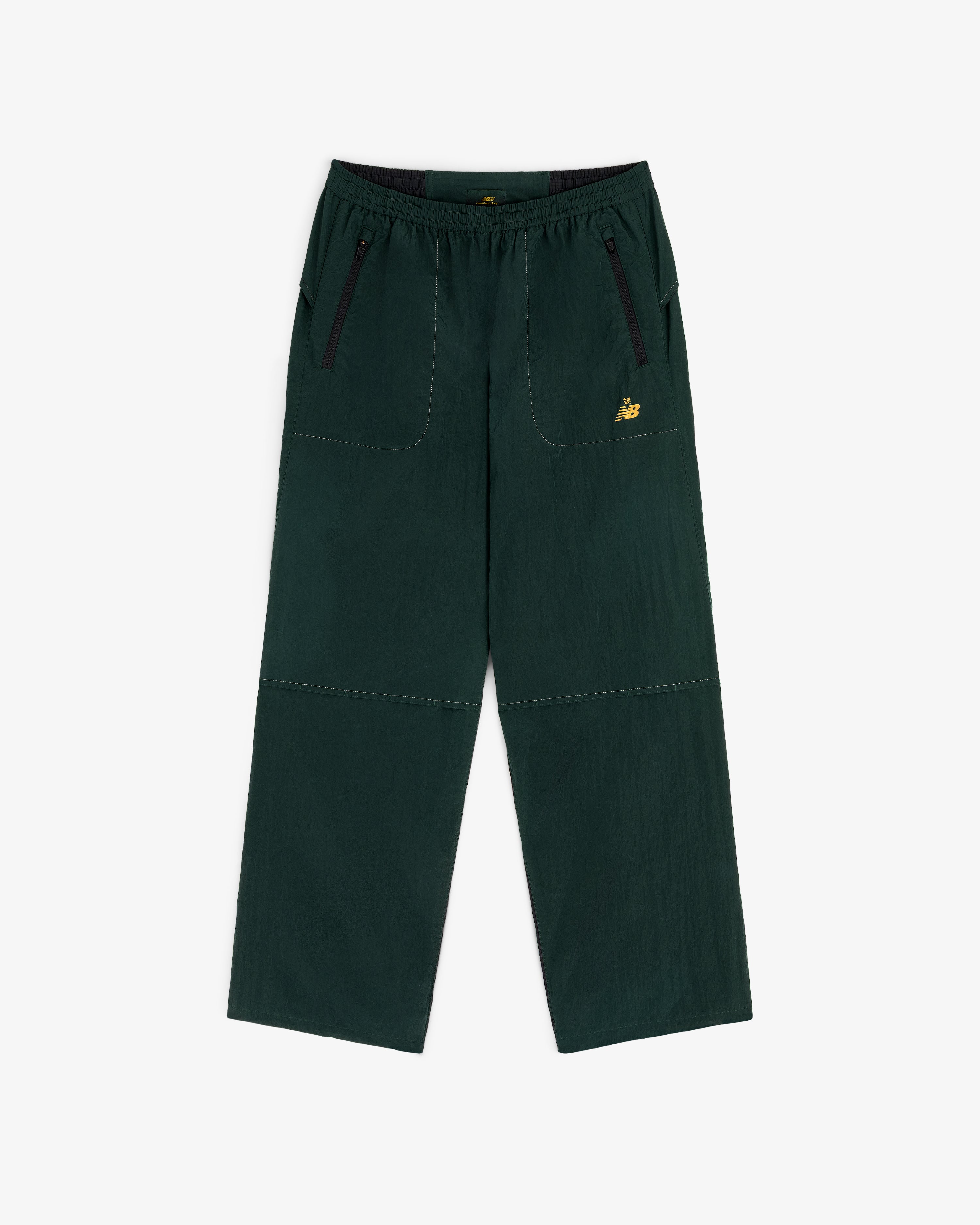 ALD / New Balance Lightweight Nylon Warmup Pant in dark green with front pockets, black zippers, and yellow NB logo.