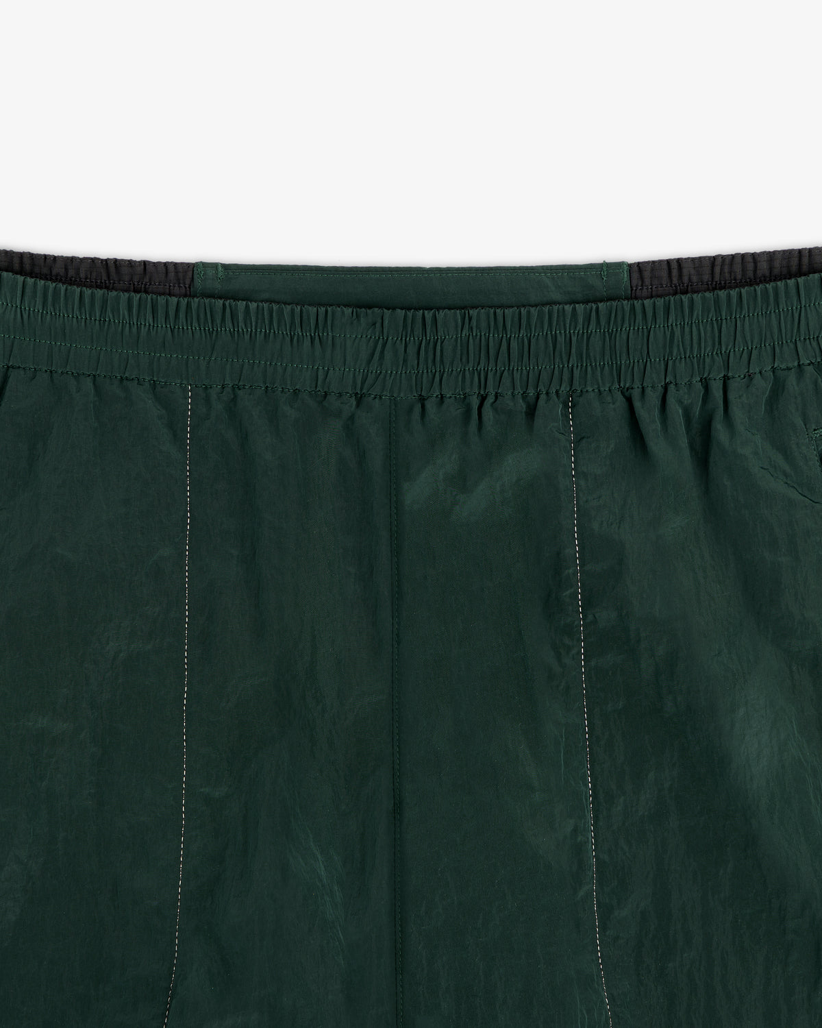 Close-up of the waistband and upper section of the ALD / New Balance Lightweight Nylon Warmup Pant in dark green.