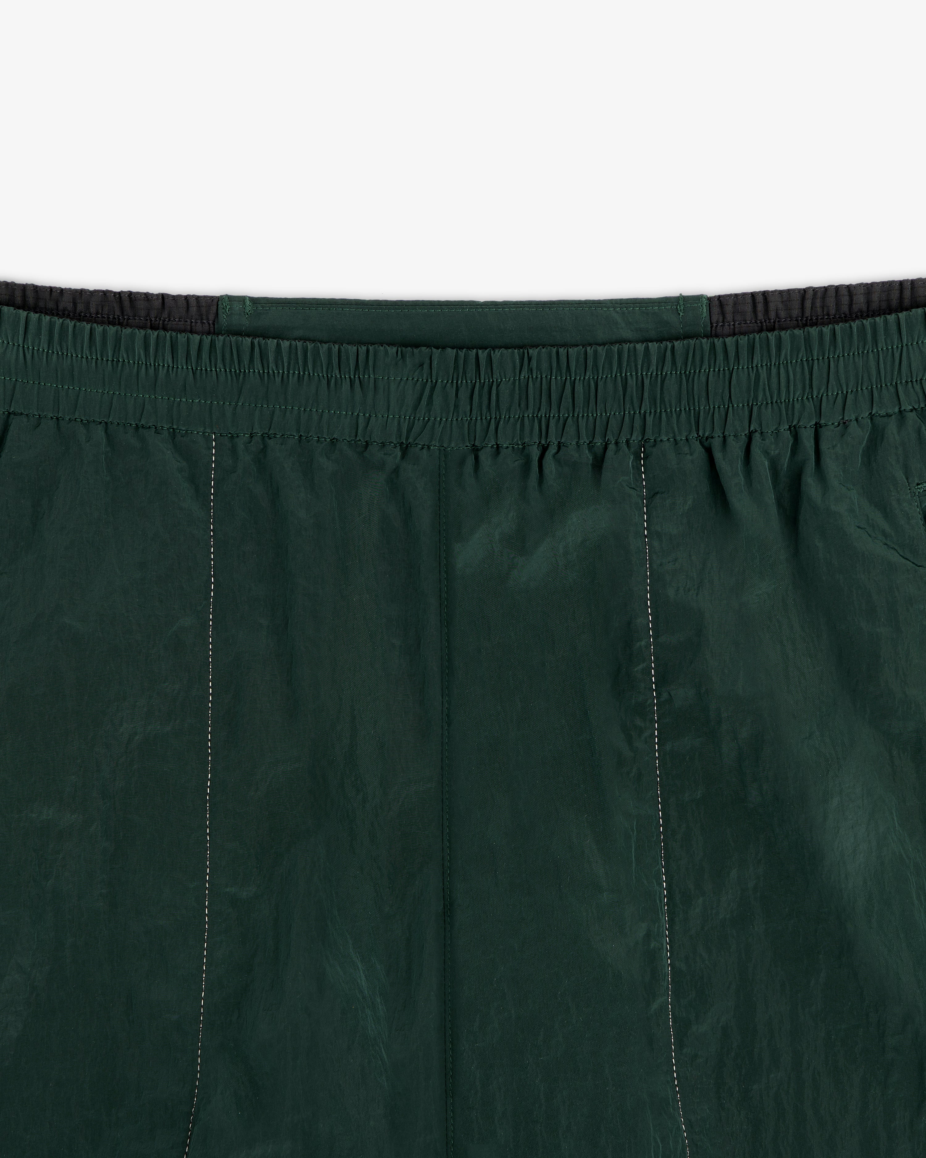 Close-up of the waistband and upper section of the ALD / New Balance Lightweight Nylon Warmup Pant in dark green.