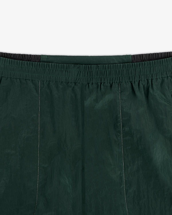 Close-up of the waistband and upper section of the ALD / New Balance Lightweight Nylon Warmup Pant in dark green.