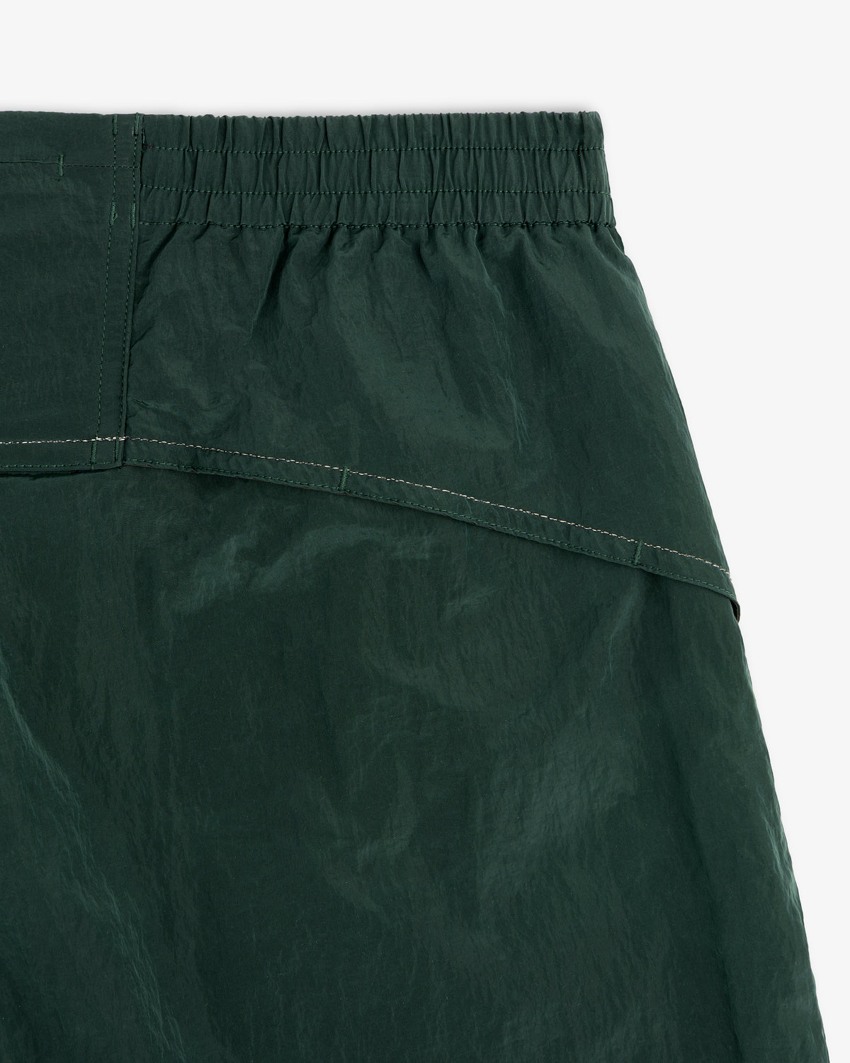 Close-up of ALD / New Balance Lightweight Nylon Warmup Pant in forest green with elastic waistband and visible stitching.