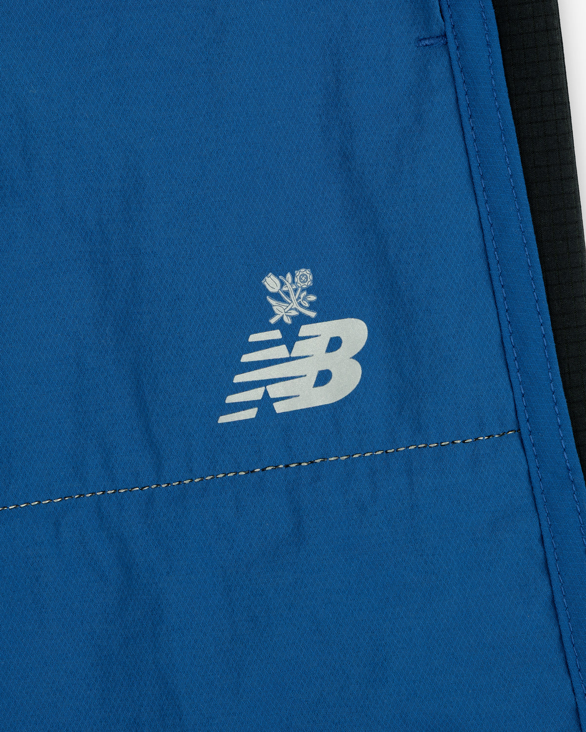 Close-up of blue ALD / New Balance Performance Lightweight Running Short with white logo and two crossed roses above it.