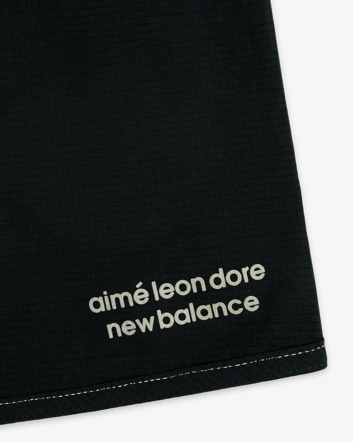 Close-up of black ALD / New Balance Performance Lightweight Running Short with white logo near hem and visible stitching.