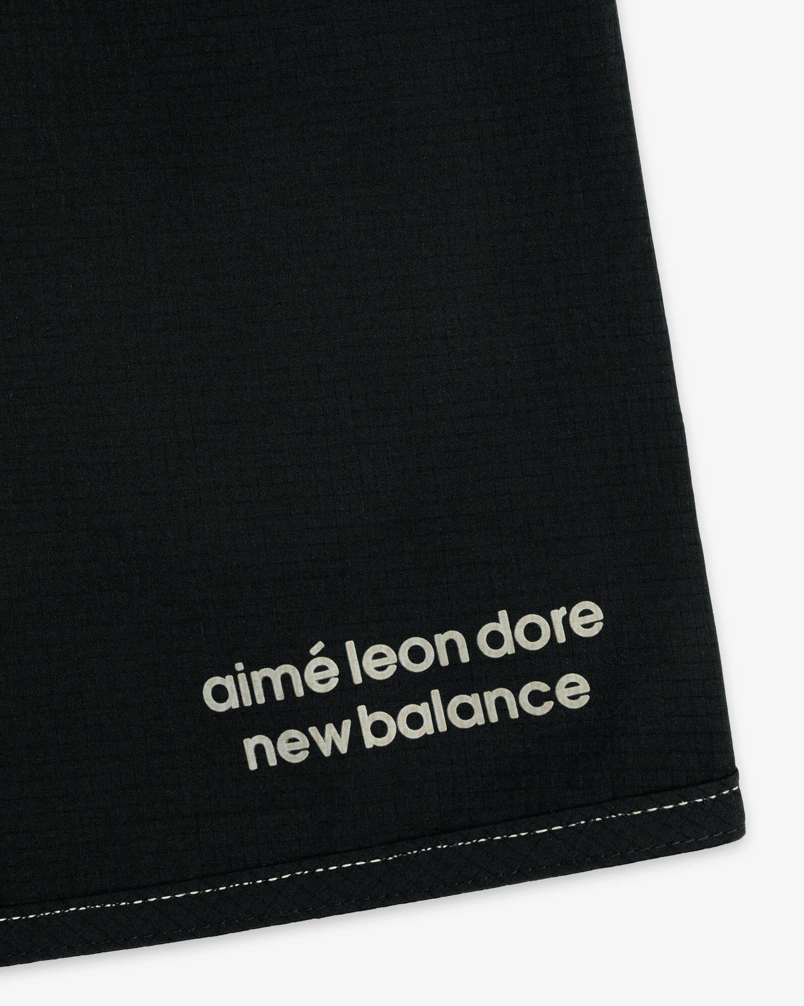 Close-up of black ALD / New Balance Performance Lightweight Running Short with white logo near hem and visible stitching.