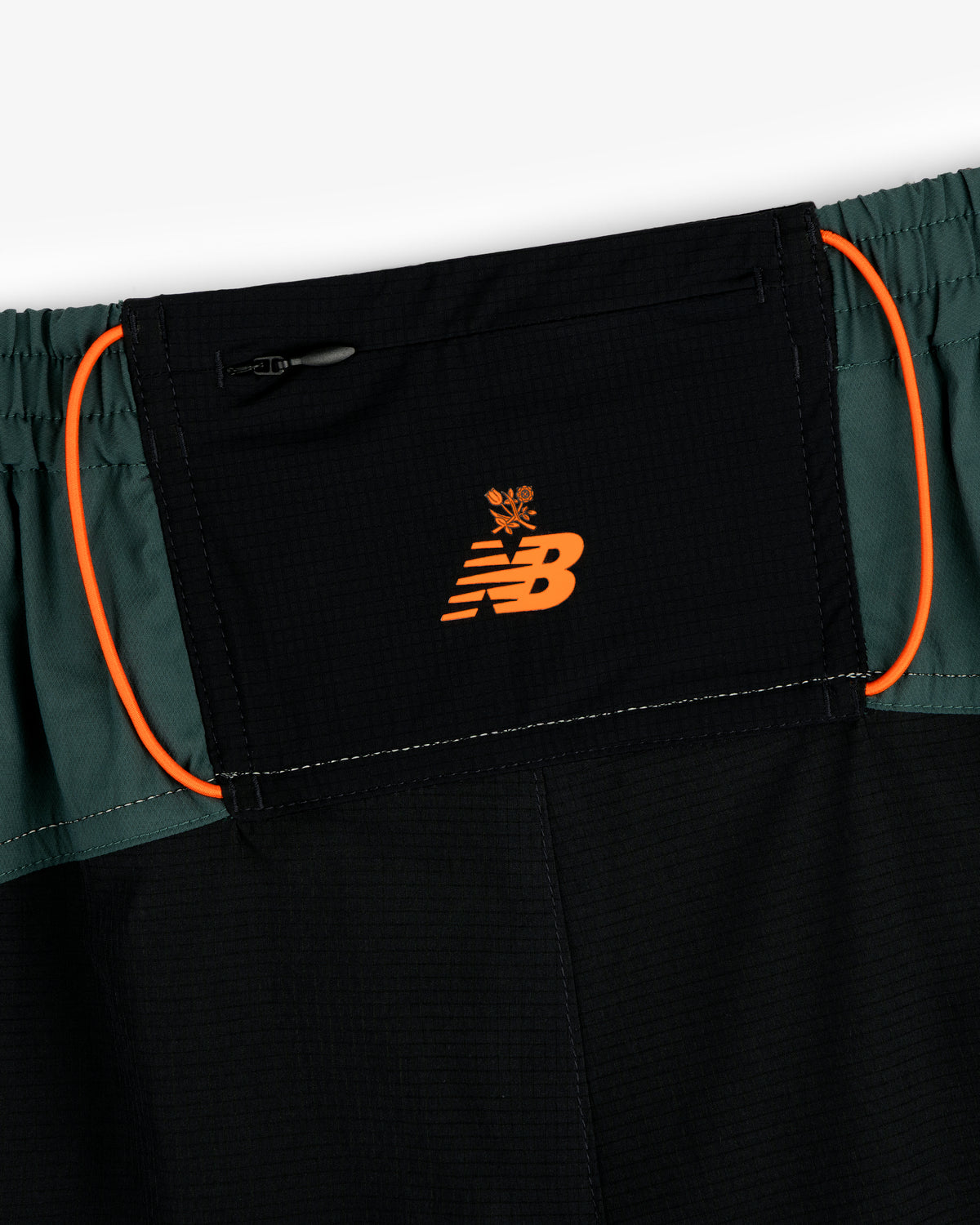 Close-up of ALD / New Balance Performance Lightweight Running Short in black and green with orange logo and trim.
