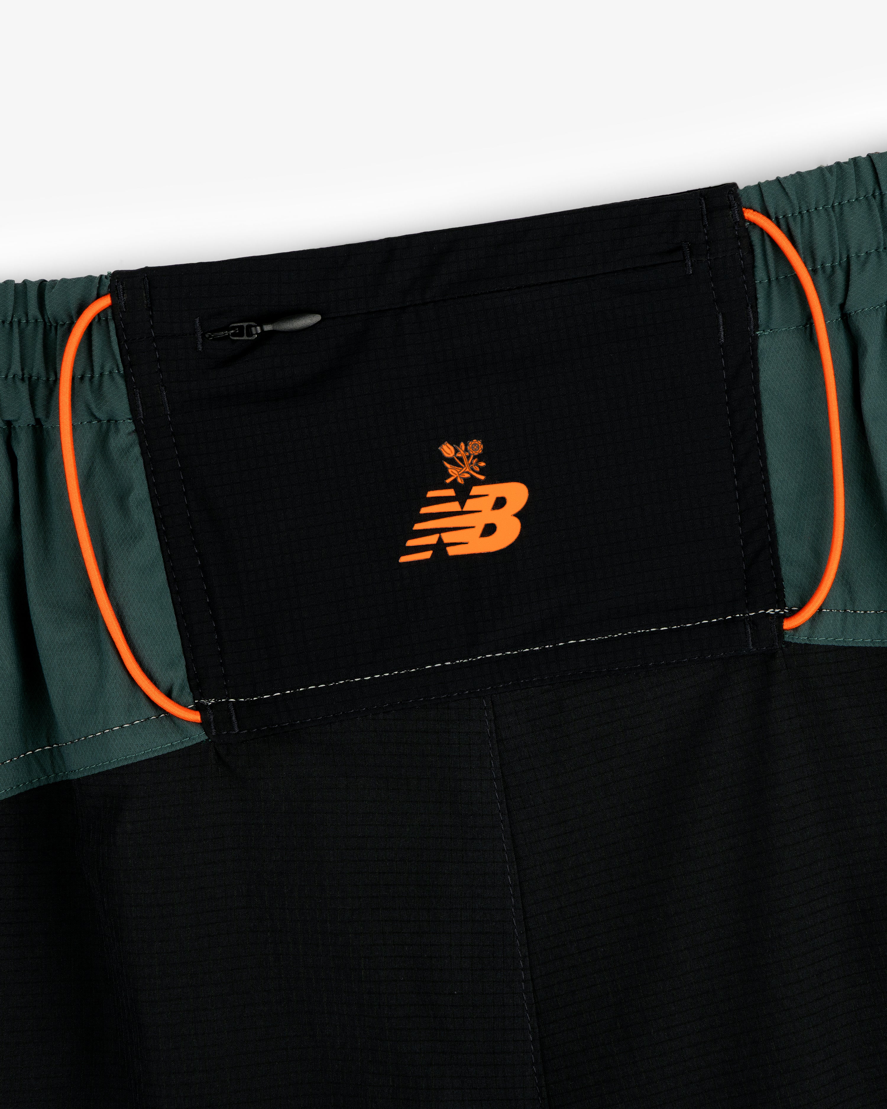 Close-up of ALD / New Balance Performance Lightweight Running Short in black and green with orange logo and trim.