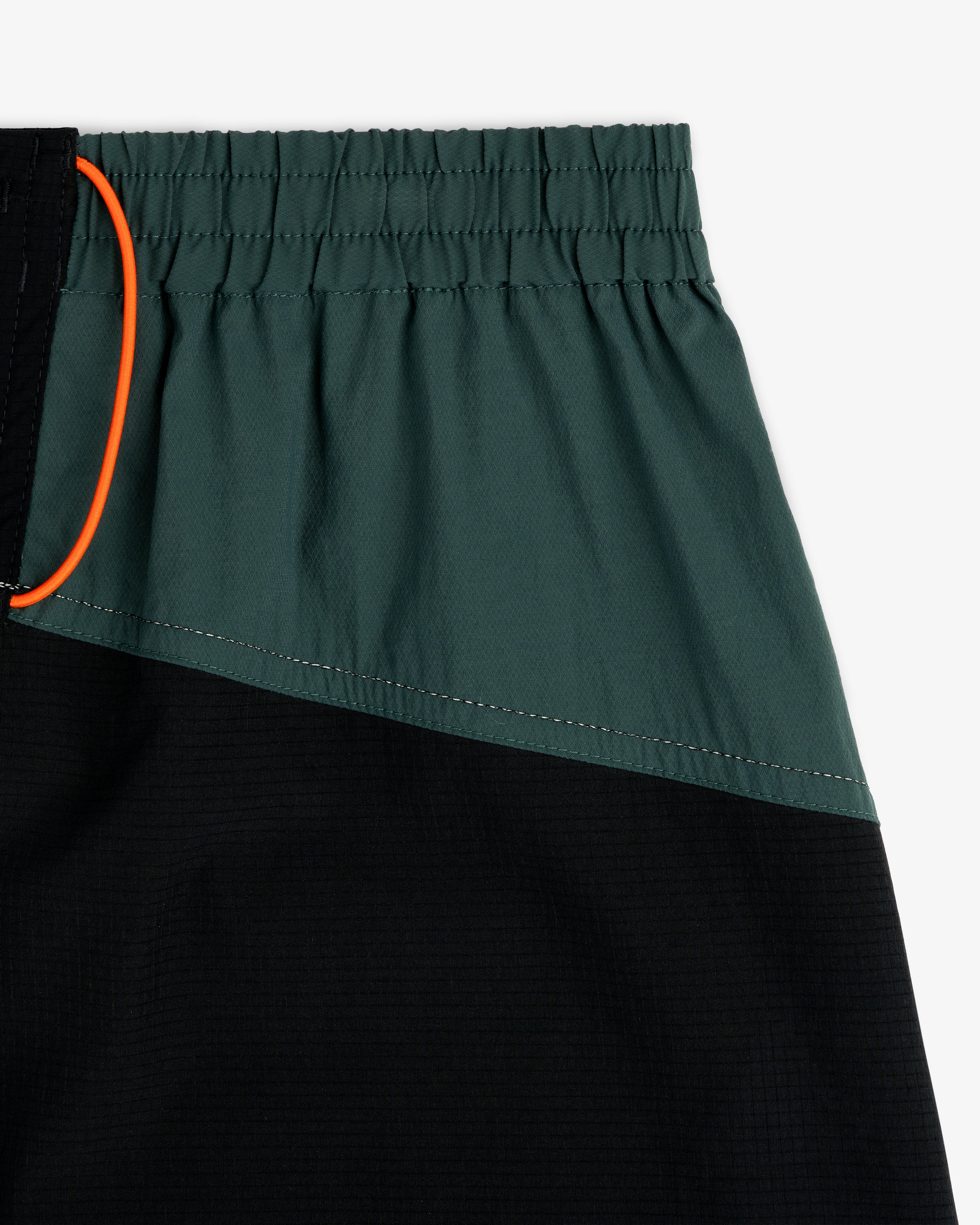 Close-up of ALD / New Balance Performance Lightweight Running Short in green and black with elastic waist and orange drawstring.