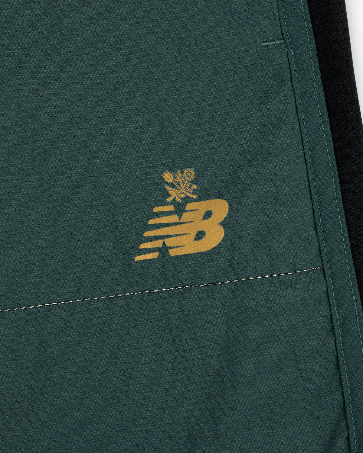 Close-up of green ALD / New Balance Performance Lightweight Running Short with yellow logo and small floral graphic.