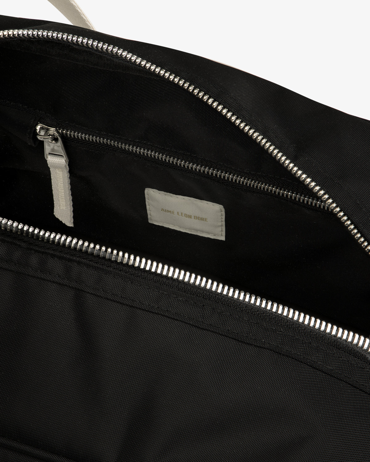 Close-up of an open Nylon Duffle Bag with a silver zipper and small inner pocket featuring a white label.