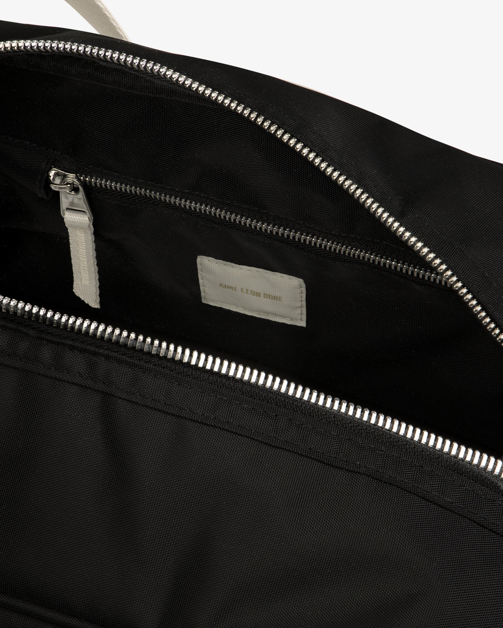 Close-up of an open Nylon Duffle Bag with a silver zipper and small inner pocket featuring a white label.